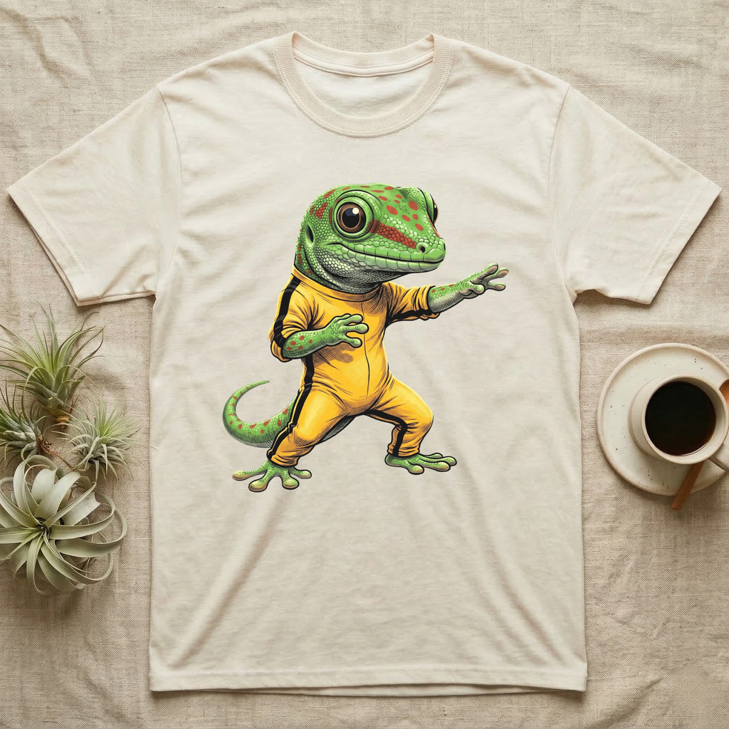 Anthropomorphic giant day gecko in a yellow-and-black martial-arts jumpsuit, low fighting stance, bold vintage-comic ink outlines and halftone shading, graphic-only design. — shown on a Natural tee.