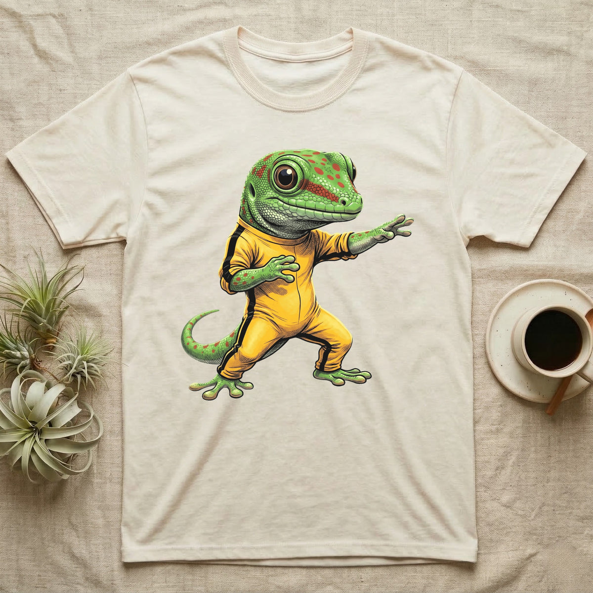 Anthropomorphic giant day gecko in a yellow-and-black martial-arts jumpsuit, low fighting stance, bold vintage-comic ink outlines and halftone shading, graphic-only design. — shown on a Natural tee.