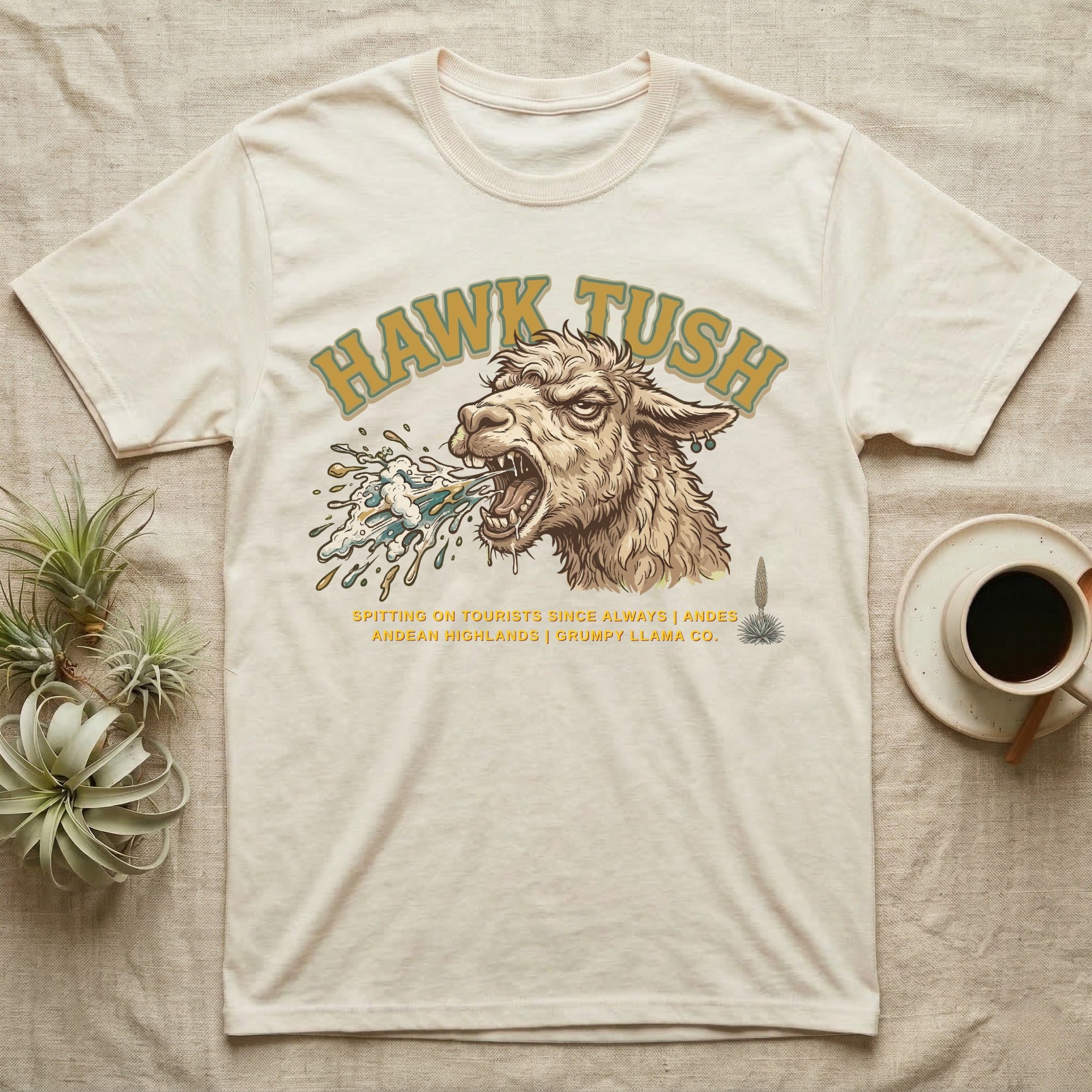 Cream t-shirt with a llama spitting, text "Hawk Tush" and "Grumpy Llama Co."