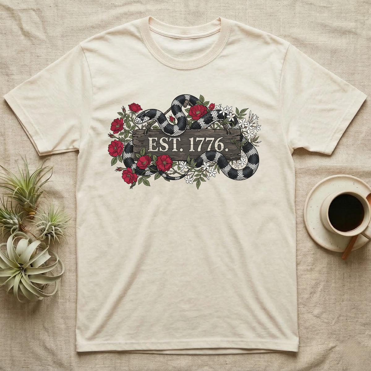 Kingsnake Floral 1776 T-Shirt in Natural — Black-and-white California kingsnake woven through roses and jasmine around a wooden sign reading Est. 1776.