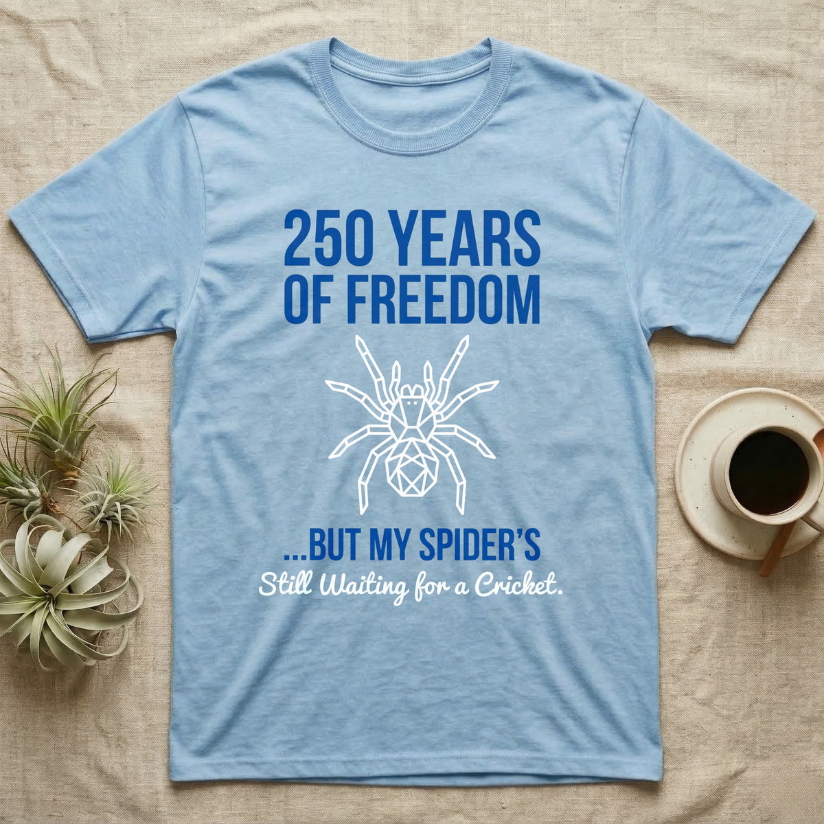Tarantula Waiting For Cricket Tee in Light Blue — Minimalist geometric tee with a low-poly white tarantula and blue text reading 250 Years Of Freedom but my spider's still waiting for a cricket.