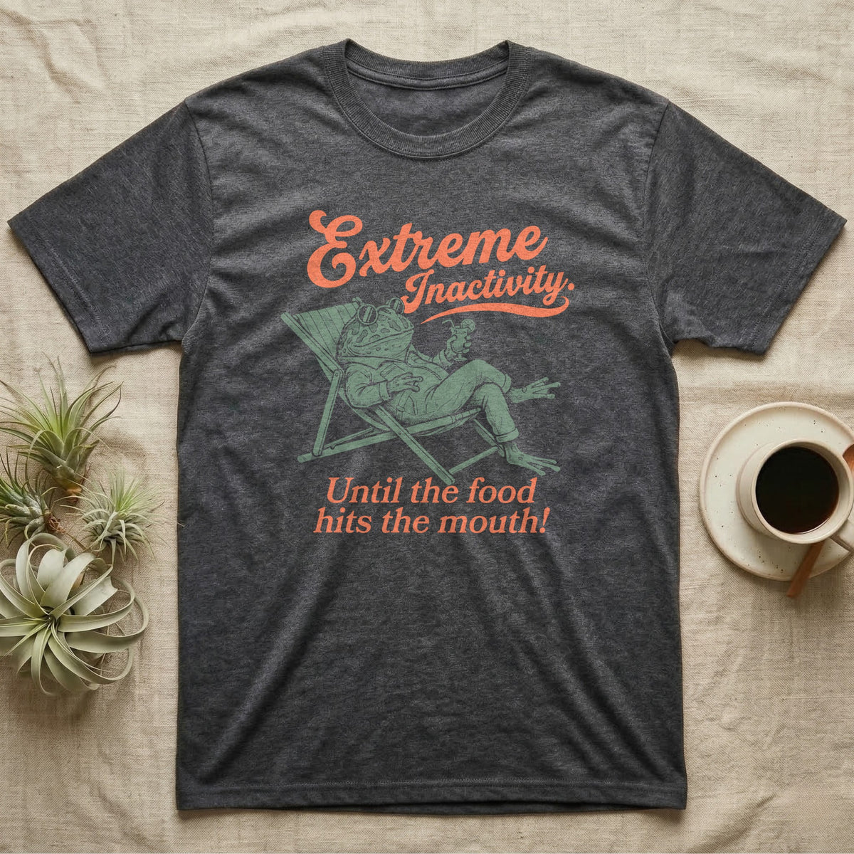 Pacman Frog Lazy Day T-Shirt in Dark Heather — Illustrated pacman frog reclining in a beach chair in a jacket with sunglasses and a cocktail, coral script reading Extreme Inactivity Until The Food Hits The Mouth.