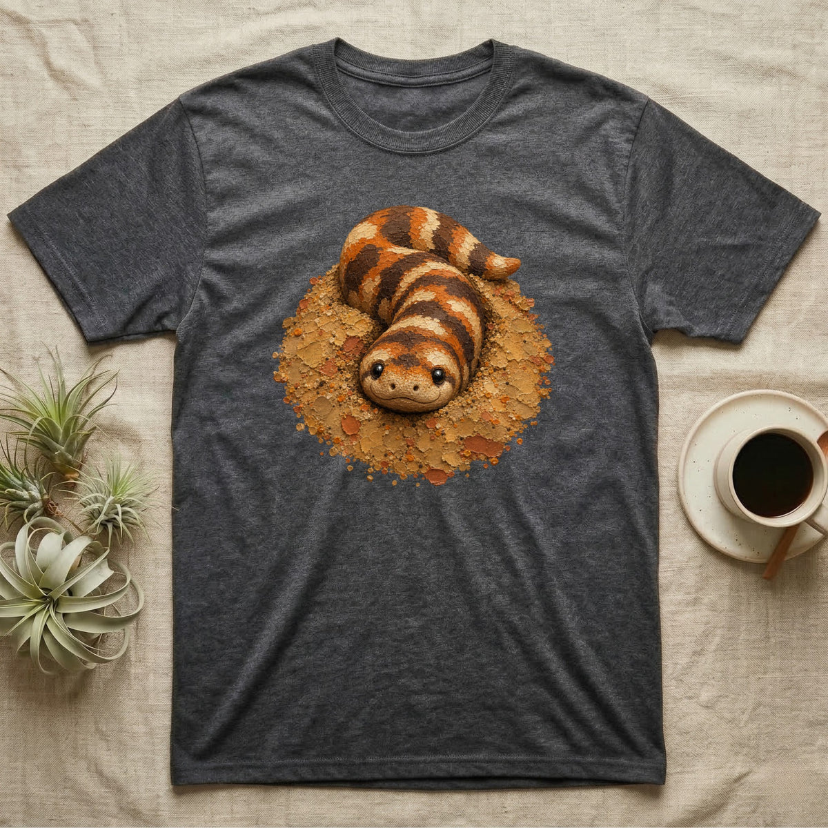 Dark gray t-shirt with a cartoon sandfish lizard design on a tan background.