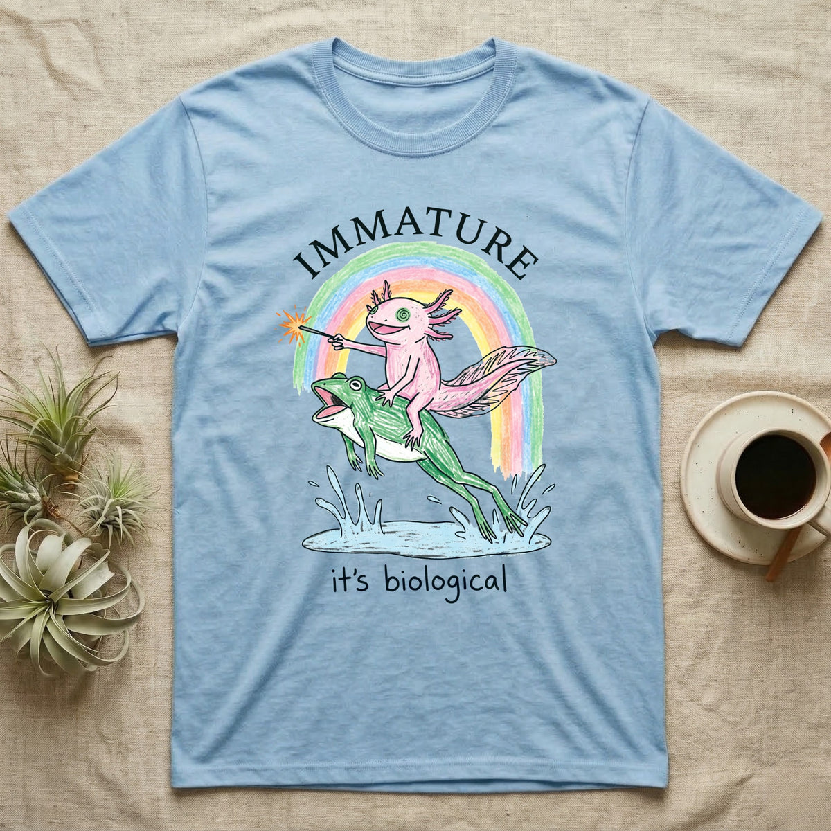 Axolotl Immature T-Shirt in Light Blue — Crayon drawing of a pink axolotl riding a leaping green frog through a rainbow, sparkler lit, under IMMATURE
