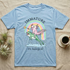 Axolotl Immature T-Shirt in Light Blue — Crayon drawing of a pink axolotl riding a leaping green frog through a rainbow, sparkler lit, under IMMATURE