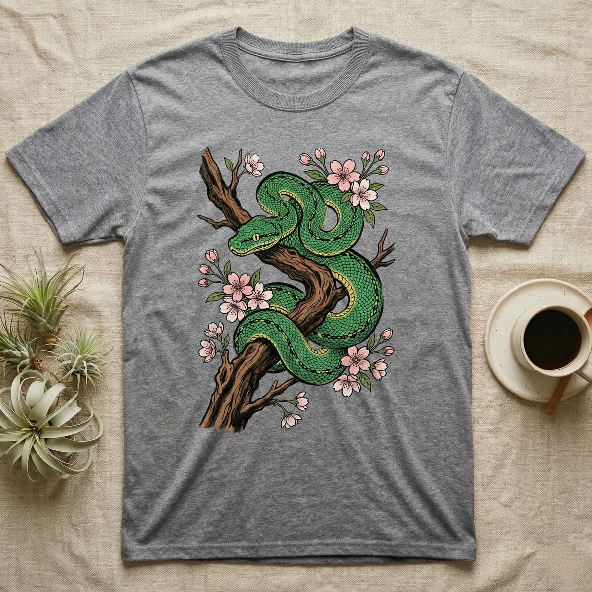 Green snake coiled on a branch with pink blossoms, on a gray t-shirt.