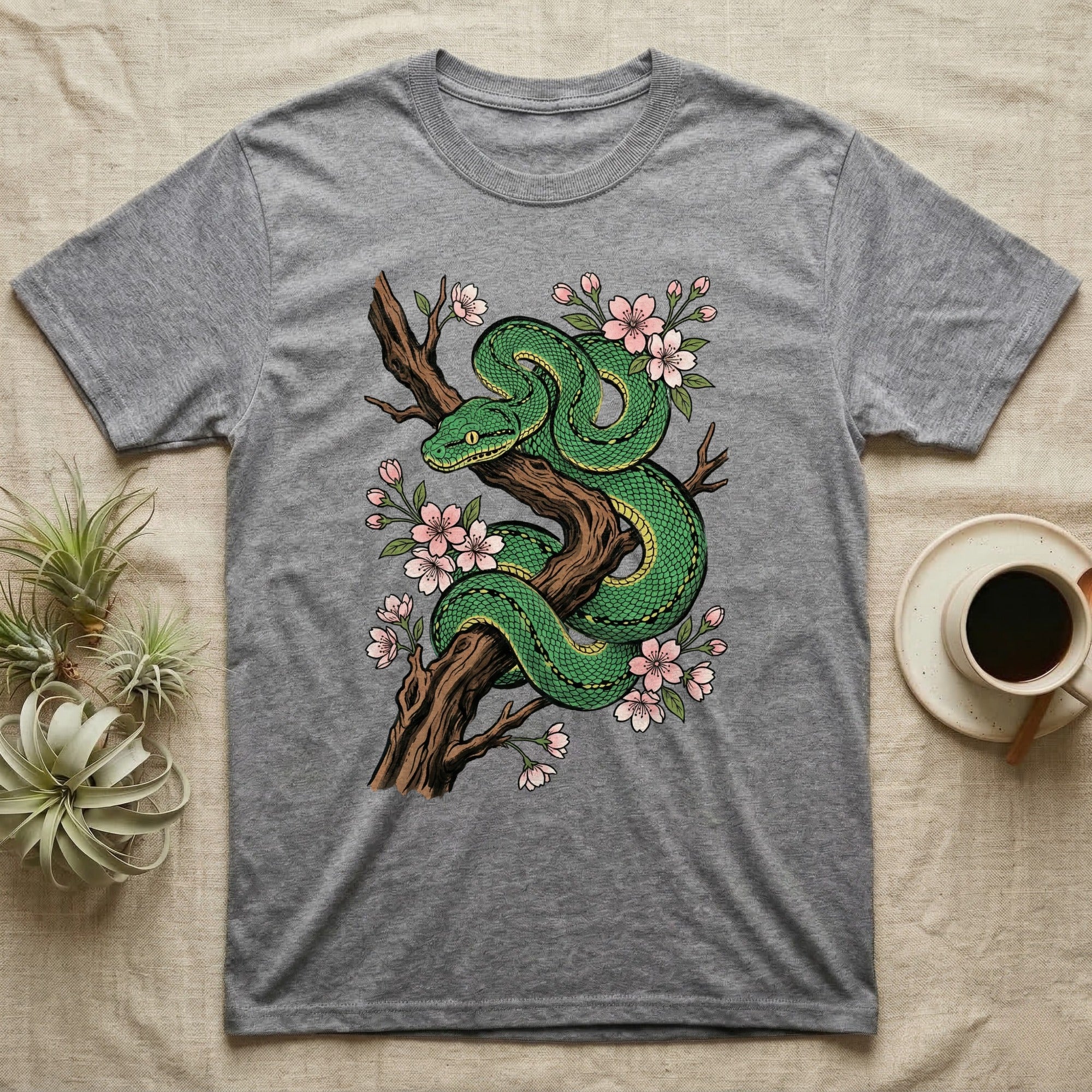 Green snake coiled on a branch with pink blossoms, on a gray t-shirt.