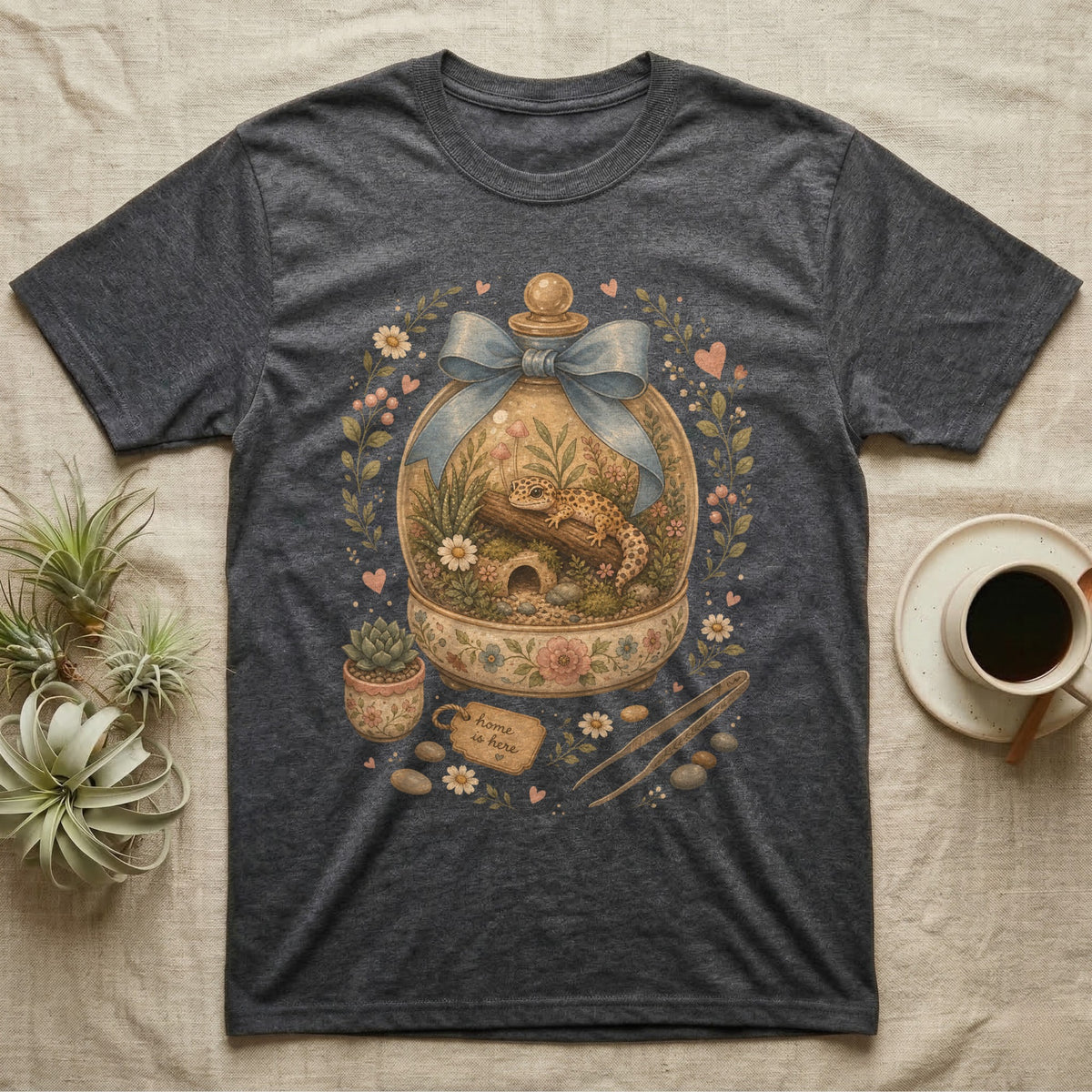 Dark t-shirt with a terrarium graphic featuring a gecko, flowers, and a "home is here" tag.