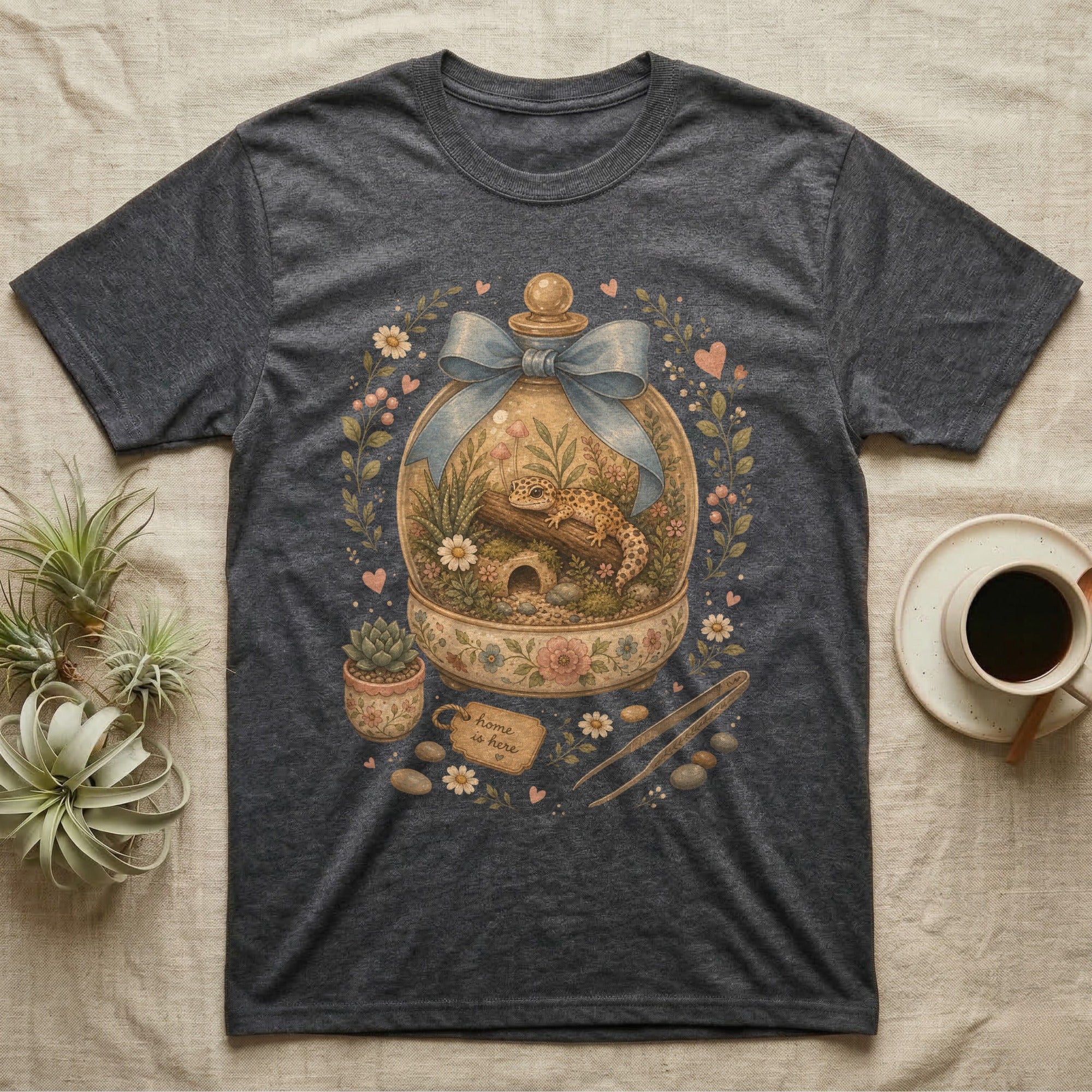 Dark t-shirt with a terrarium graphic featuring a gecko, flowers, and a "home is here" tag.