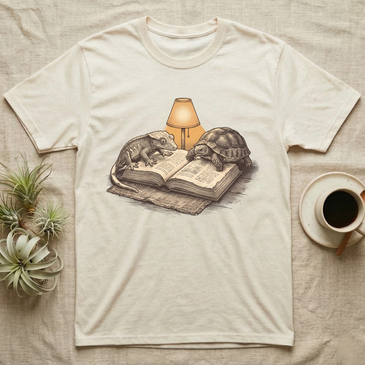 Cold-Blooded Book Club T-Shirt in Natural — Engraved cozy illustration of a gecko and a tortoise sharing an open book under a glowing reading lamp.
