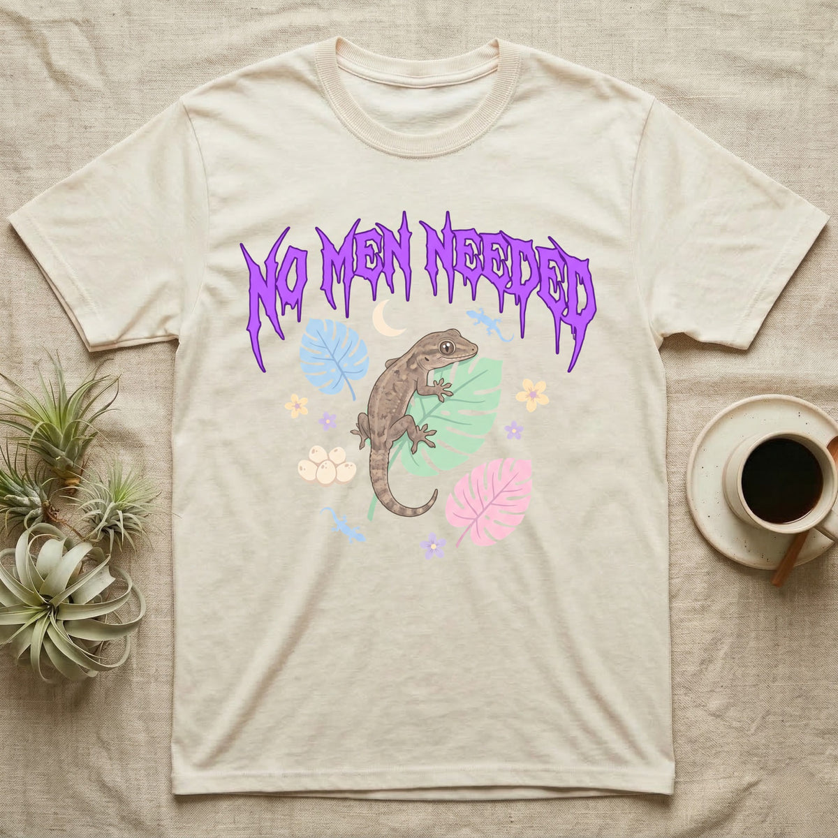 Mourning Gecko Feral T-Shirt in Natural — Mourning gecko on a leaf flanked by clone silhouettes under a jagged violet metal "NO MEN NEEDED" wordmark.
