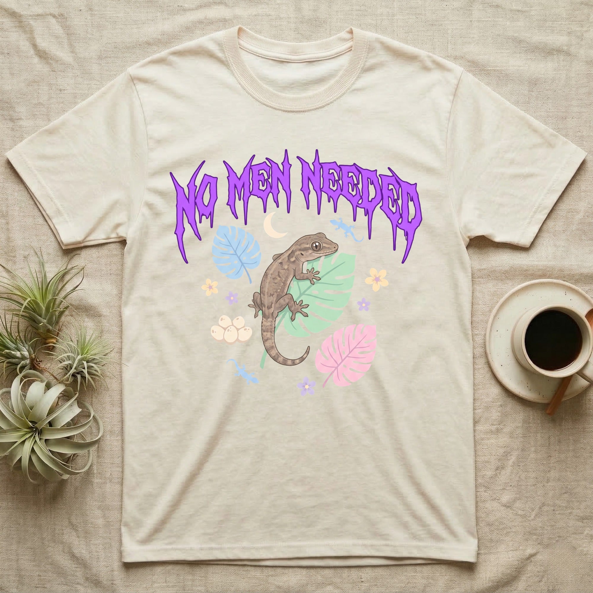 Mourning Gecko Feral T-Shirt in Natural — Mourning gecko on a leaf flanked by clone silhouettes under a jagged violet metal "NO MEN NEEDED" wordmark.