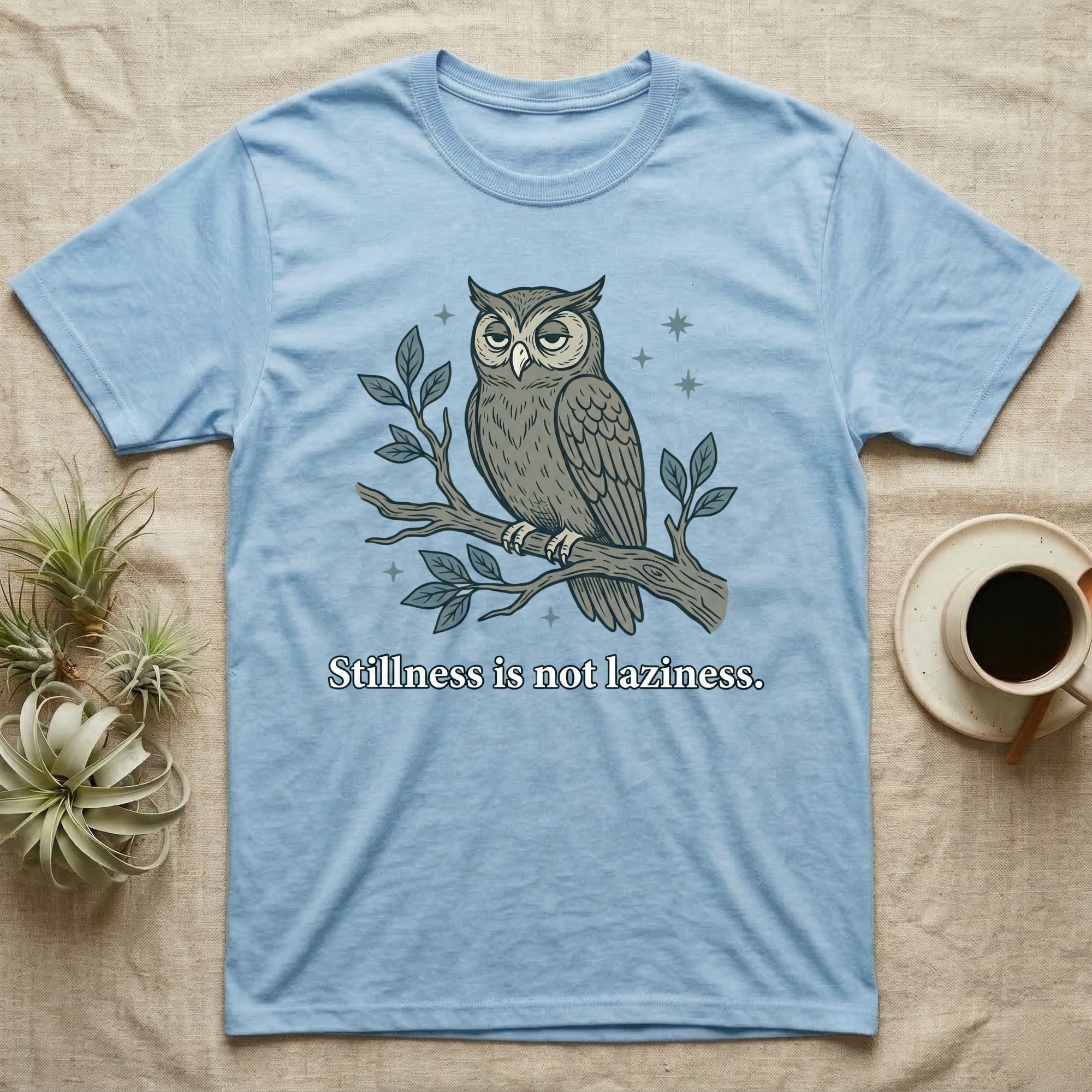Light blue t-shirt with a stylized owl on a branch and the text "Stillness is not laziness."