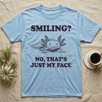 Axolotl Resting Face T-Shirt in Light Blue — Engraved axolotl sitting head-on with gills fanned and a wide smile, with the words Smiling? No, That's Just My Face