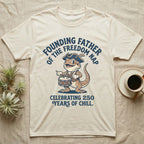 Bearded Dragon Freedom Nap T-Shirt in Natural — Cartoon bearded dragon as a drummer boy under arched text Founding Father of the Freedom Nap, 250 Years of Chill.