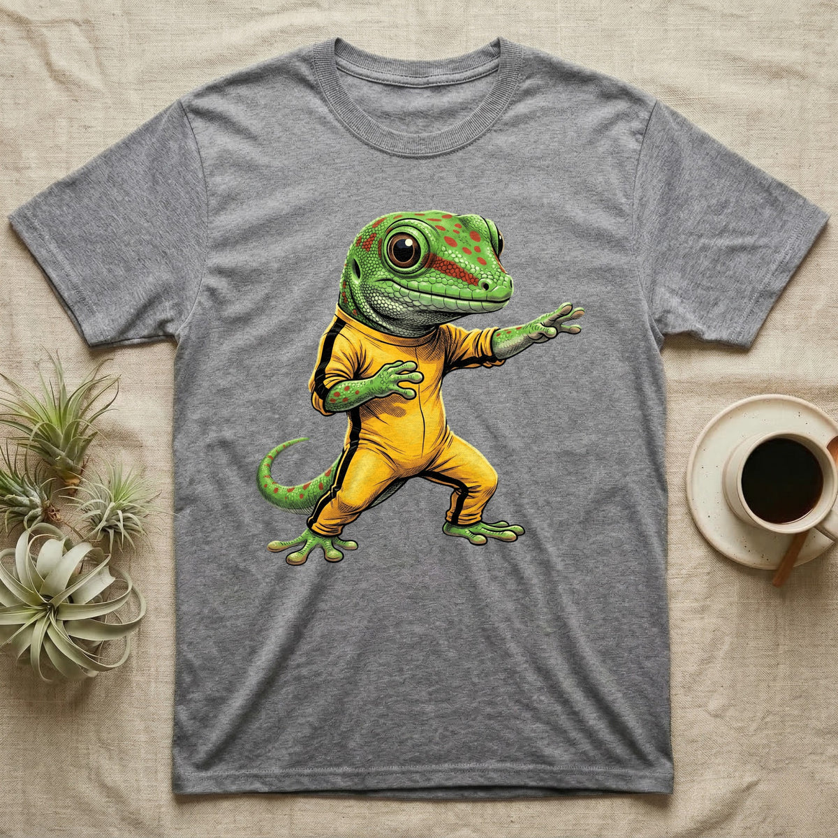 Anthropomorphic giant day gecko in a yellow-and-black martial-arts jumpsuit, low fighting stance, bold vintage-comic ink outlines and halftone shading, graphic-only design. — shown on a Sport Grey tee.