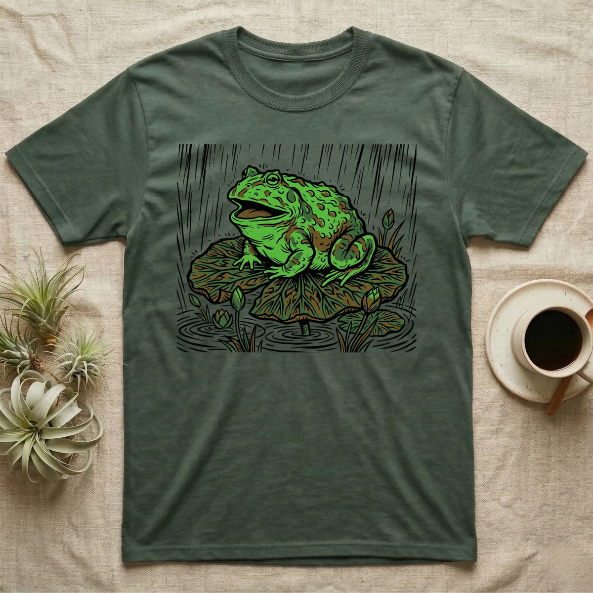 Green t-shirt featuring a large frog sitting on a lily pad in the rain.