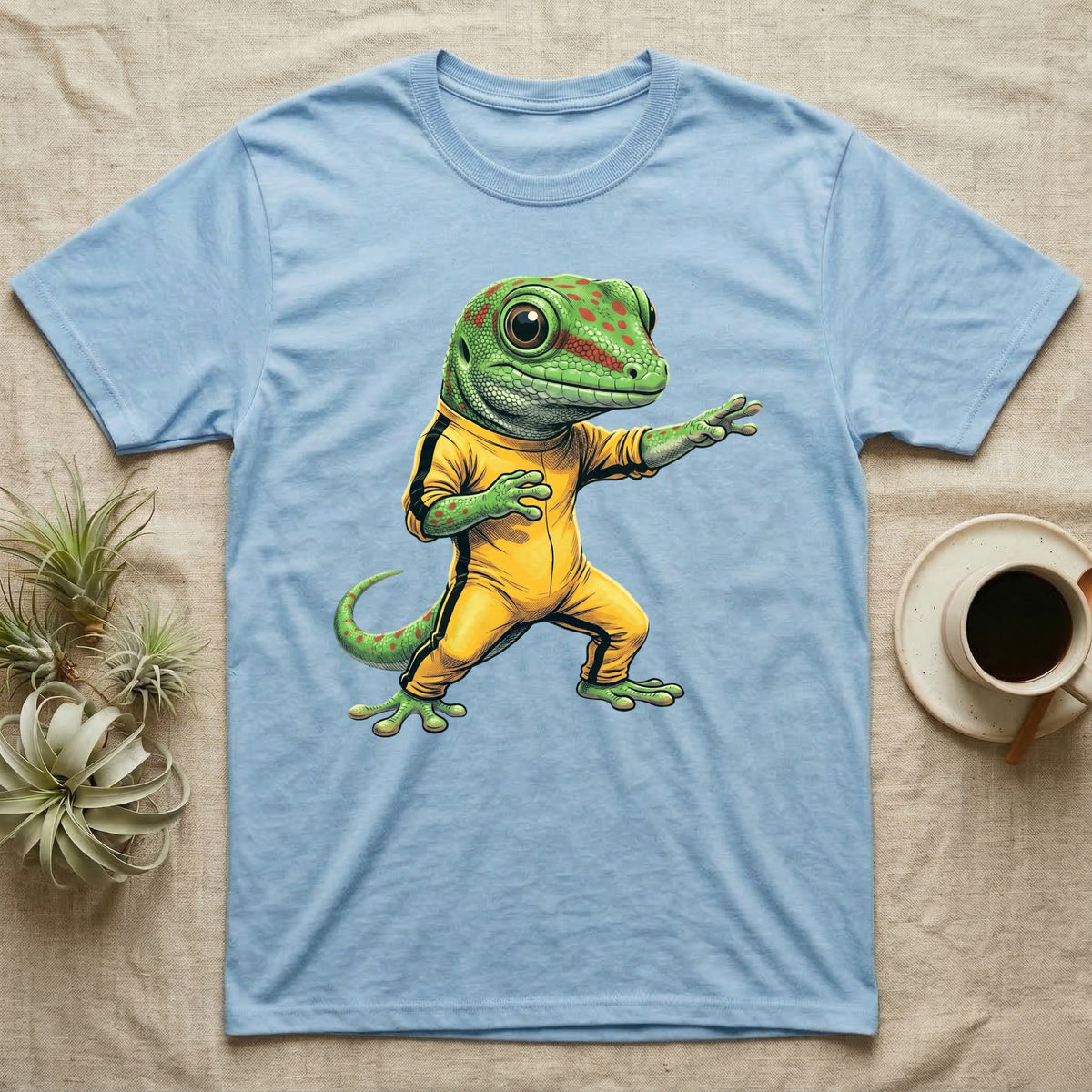 Anthropomorphic giant day gecko in a yellow-and-black martial-arts jumpsuit, low fighting stance, bold vintage-comic ink outlines and halftone shading, graphic-only design. — shown on a Light Blue tee.