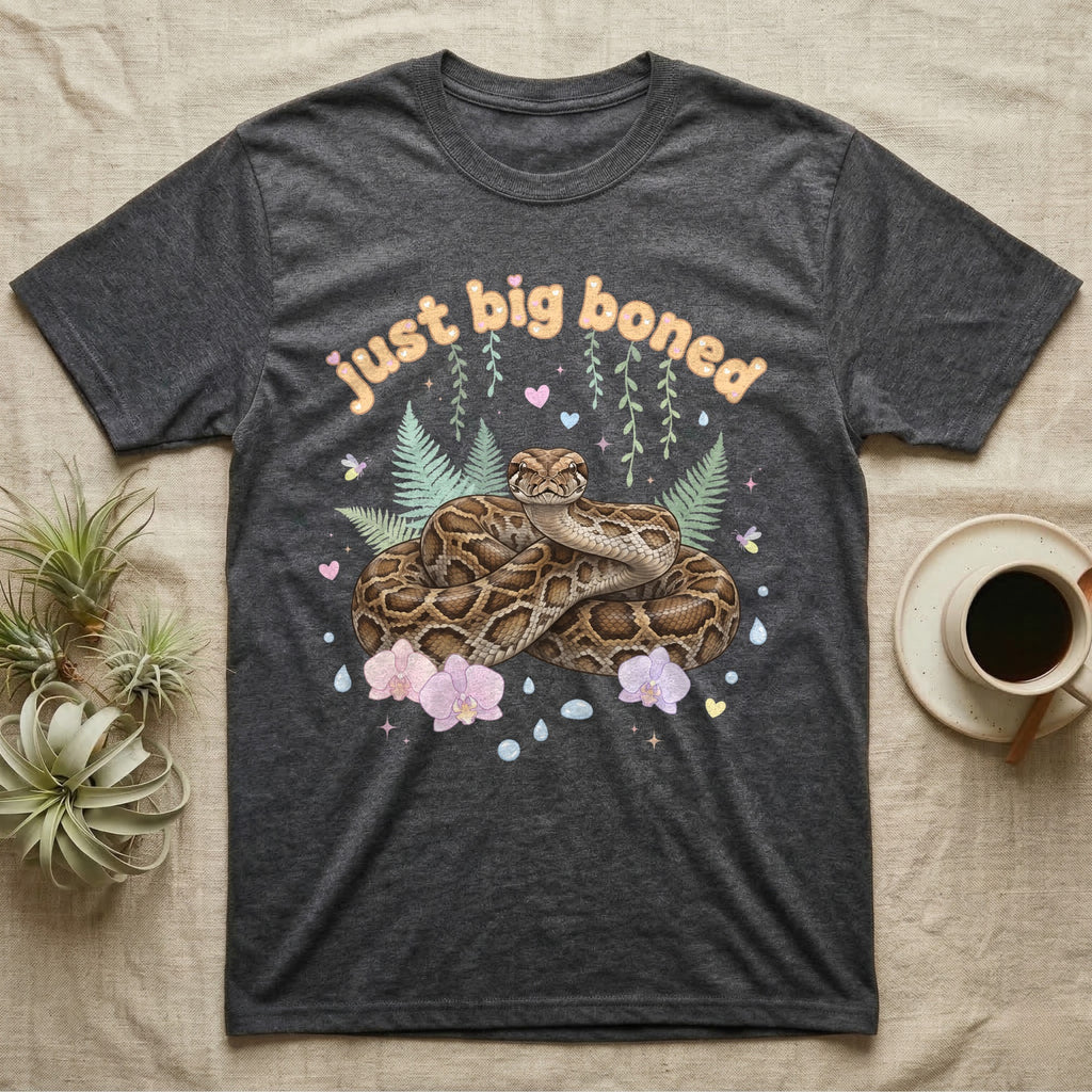 Burmese Python Baby T-Shirt in Dark Heather — Massive coiled Burmese python among pastel ferns and orchids under puffy butterscotch bubble text "just big boned".