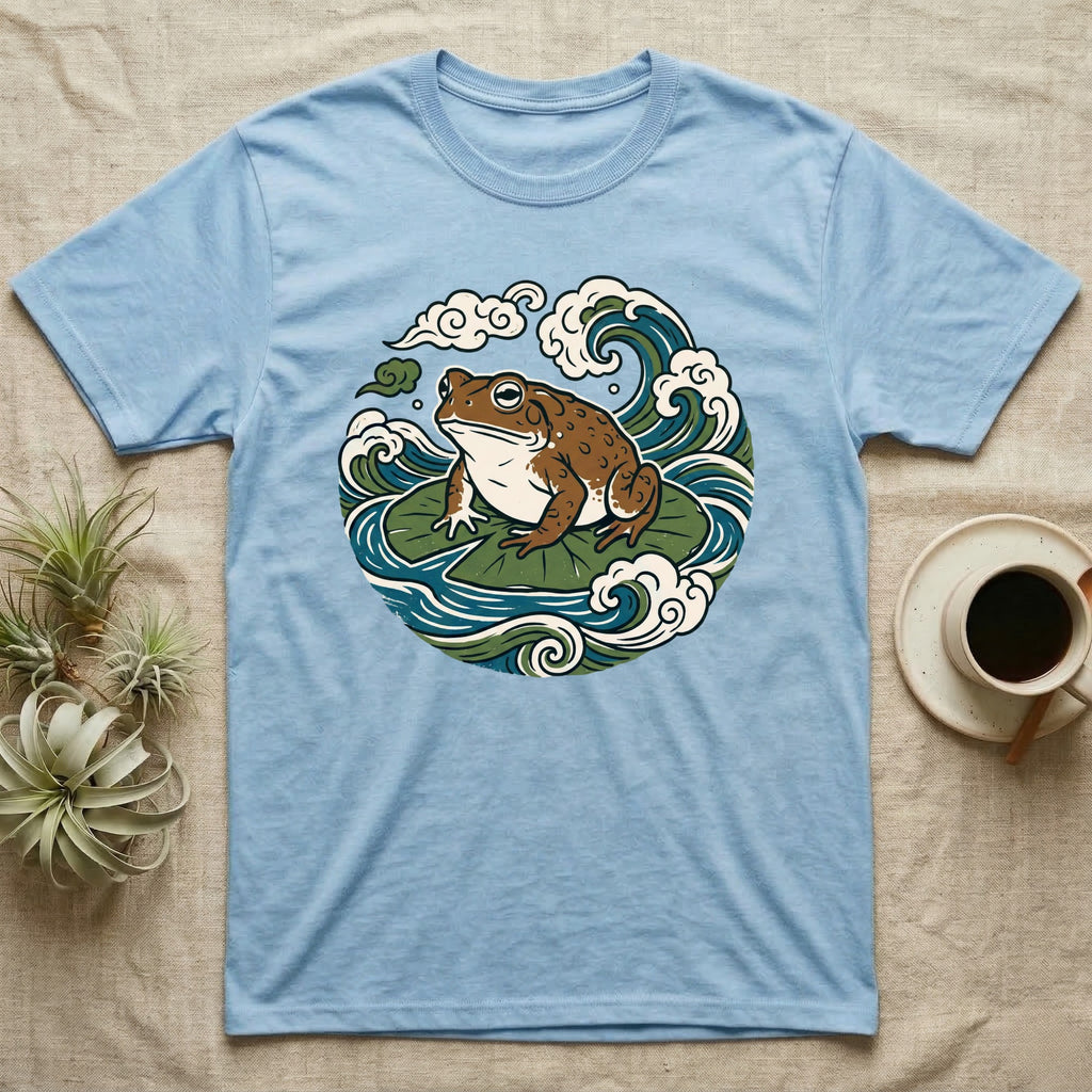 Frog sitting on lily pads with waves and clouds design on light blue t-shirt.