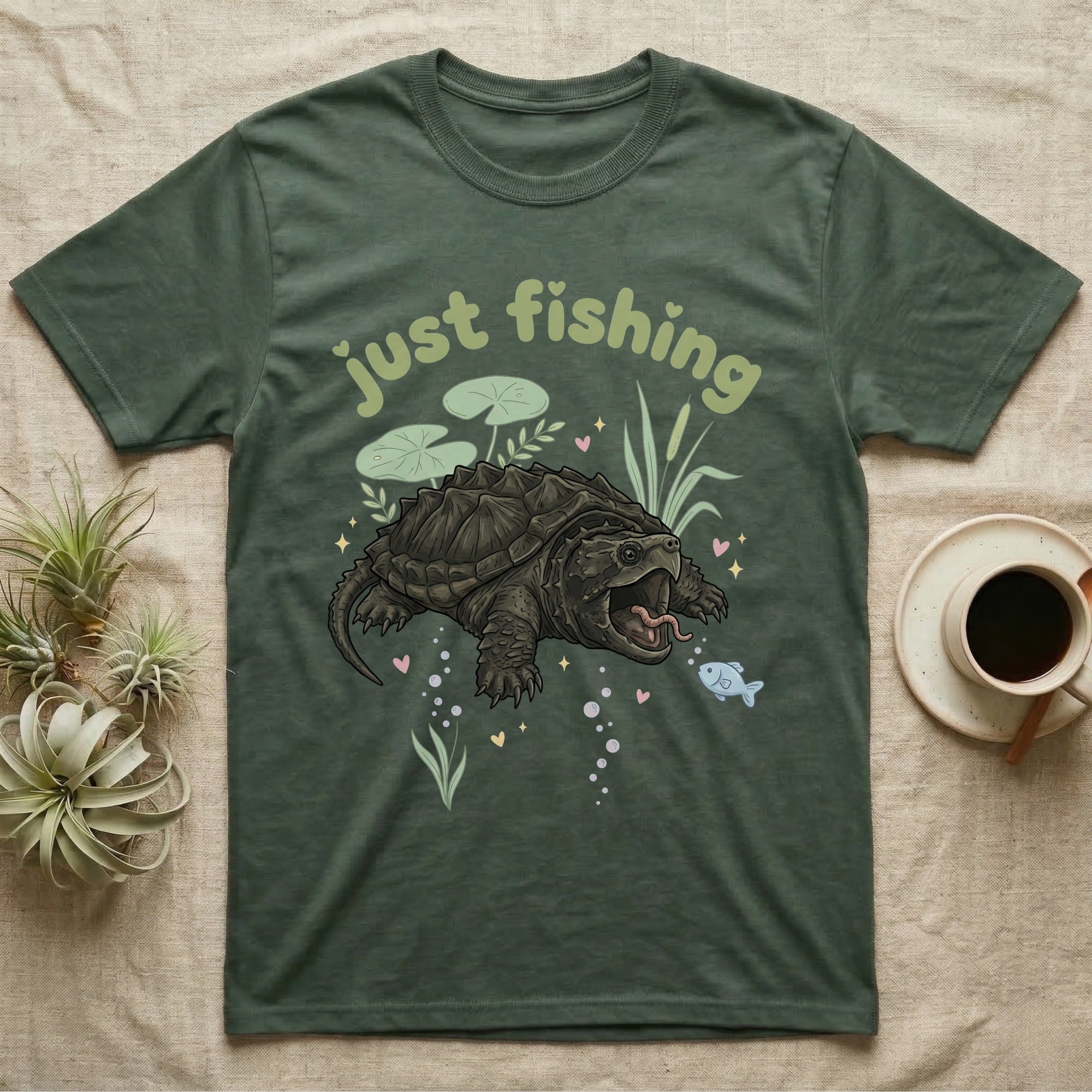 Alligator Snapping Turtle Softie T-Shirt in Military Green — Alligator snapping turtle with open mouth and tongue lure under a puffy pastel "just fishing" bubble wordmark.