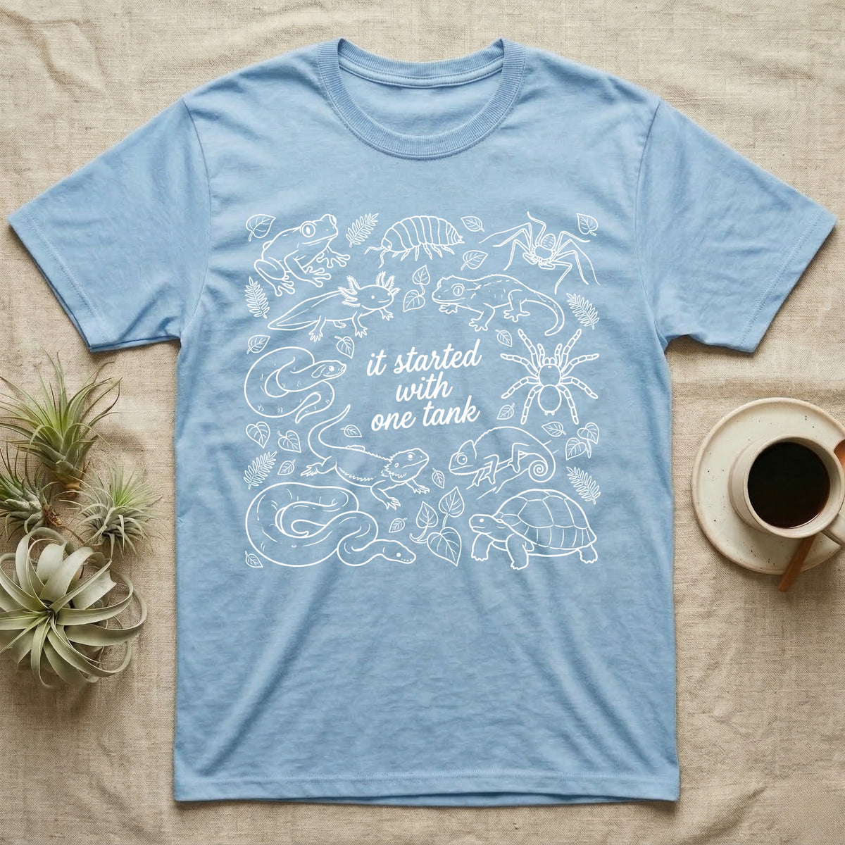 Terrarium Keeper One Tank T-Shirt in Light Blue — White outline illustration of eleven terrarium species — bearded dragon, crested gecko, ball python, axolotl, tortoise, tarantula, isopod, whip spider, chameleon, tree frog and hognose — with pothos and fern leaves, ringed around the script line it started with one tank.