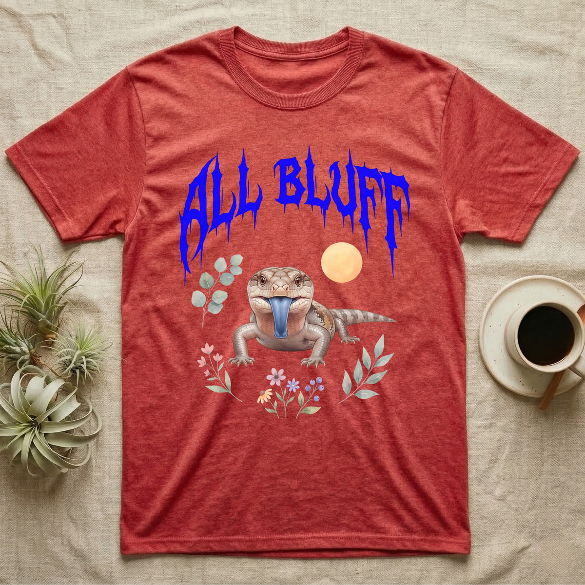 Northern Blue-Tongue Skink Feral T-Shirt in Heather Red — Blue-tongue skink with its blue tongue out under a jagged cobalt-blue metal "ALL BLUFF" wordmark and pastel leaves.