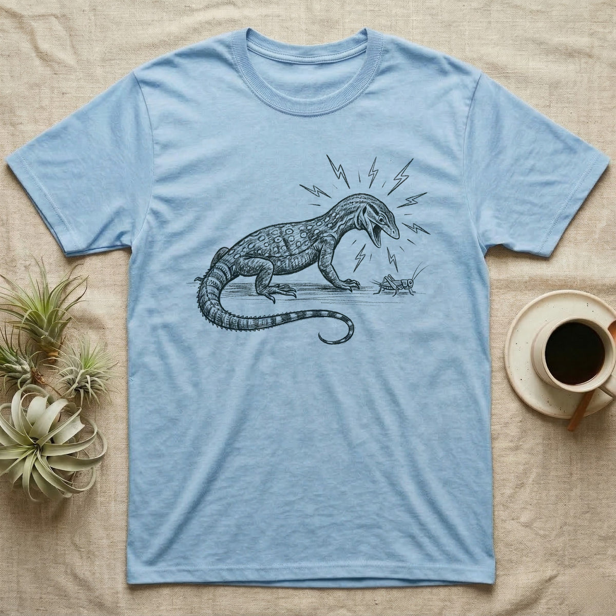 Ackie Monitor Meltdown T-Shirt in Light Blue — A charcoal drawing of an ackie monitor hissing furiously at one small, calm cricket, with lightning bolts around its head.