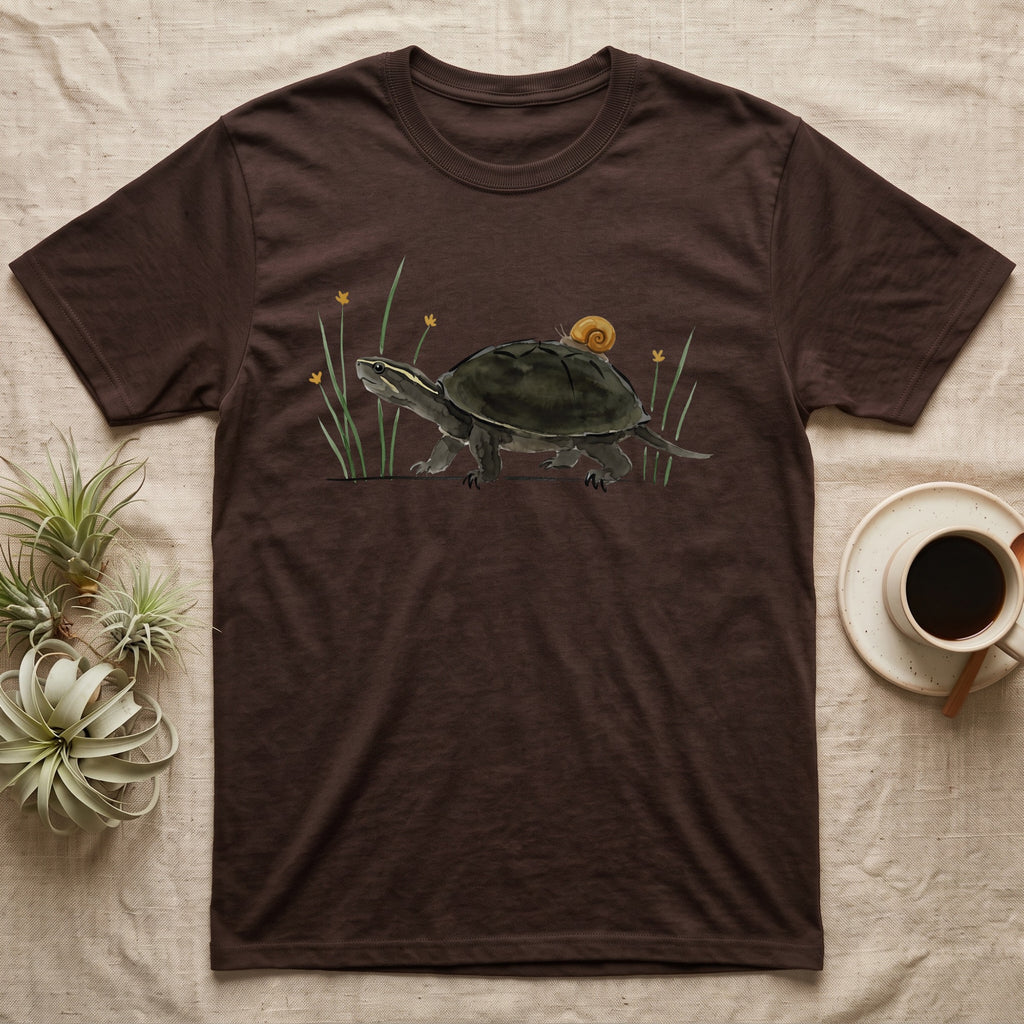 Musk Turtle Hitchhiker T-Shirt in Dark Chocolate — Watercolour musk turtle walking left with a ramshorn snail on its shell, beside slender grass blades with tiny amber flowers.