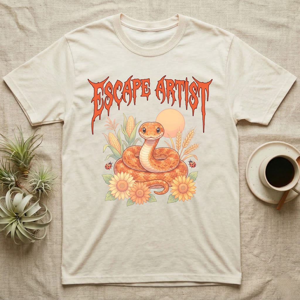 Corn Snake Feral T-Shirt in Natural — Orange corn snake coiled in a pastel cornfield scene under a spiky blood-orange metal wordmark reading ESCAPE ARTIST.