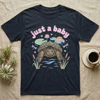 Common Snapping Turtle Baby T-Shirt in Navy — Snapping turtle with hooked beak and spiky shell among pastel lily pads under puffy pink bubble text "just a baby".