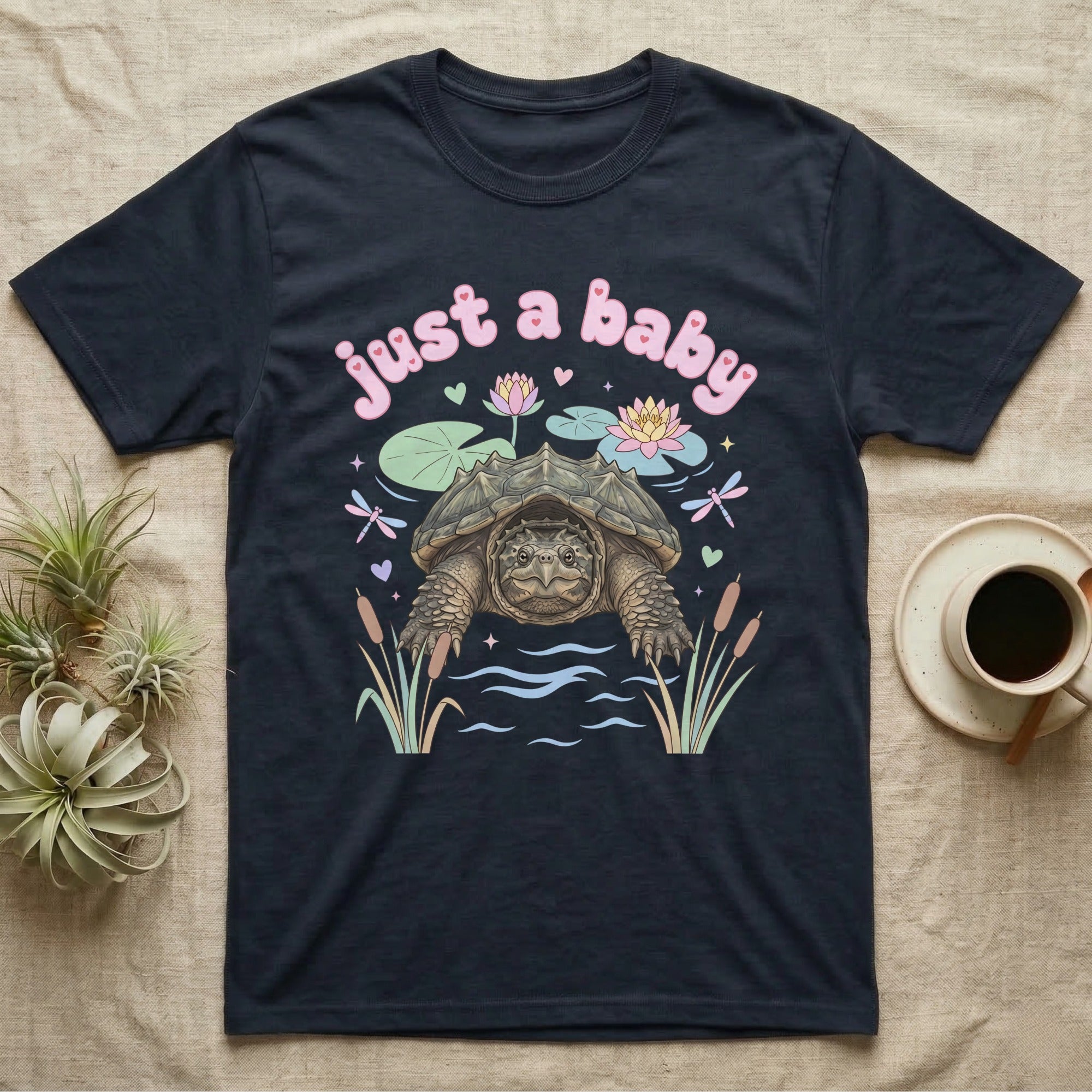 Common Snapping Turtle Baby T-Shirt in Navy — Snapping turtle with hooked beak and spiky shell among pastel lily pads under puffy pink bubble text "just a baby".