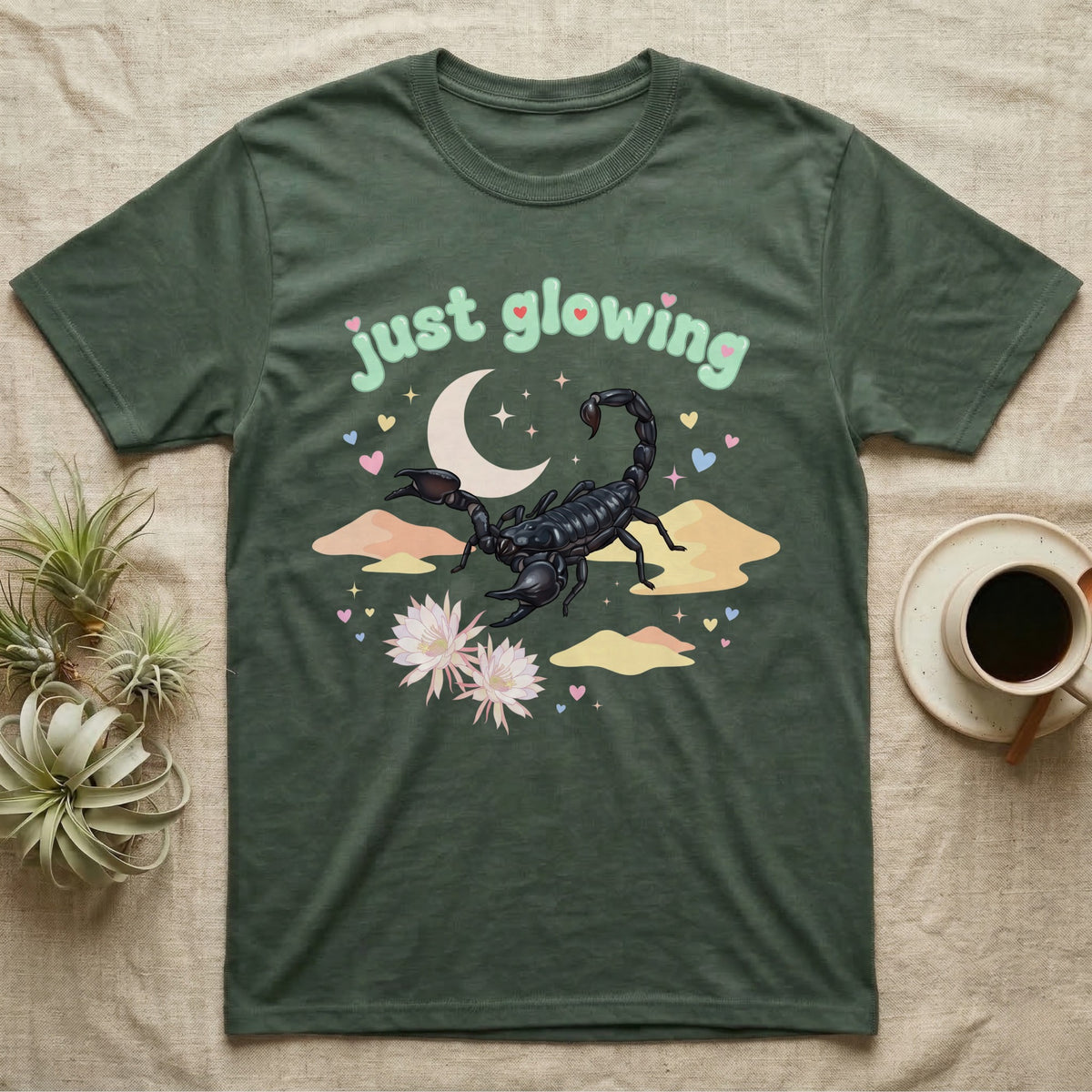 Emperor Scorpion Baby T-Shirt in Military Green — Black emperor scorpion, pincers raised, under a pastel moon and stars with puffy mint bubble text "just glowing".