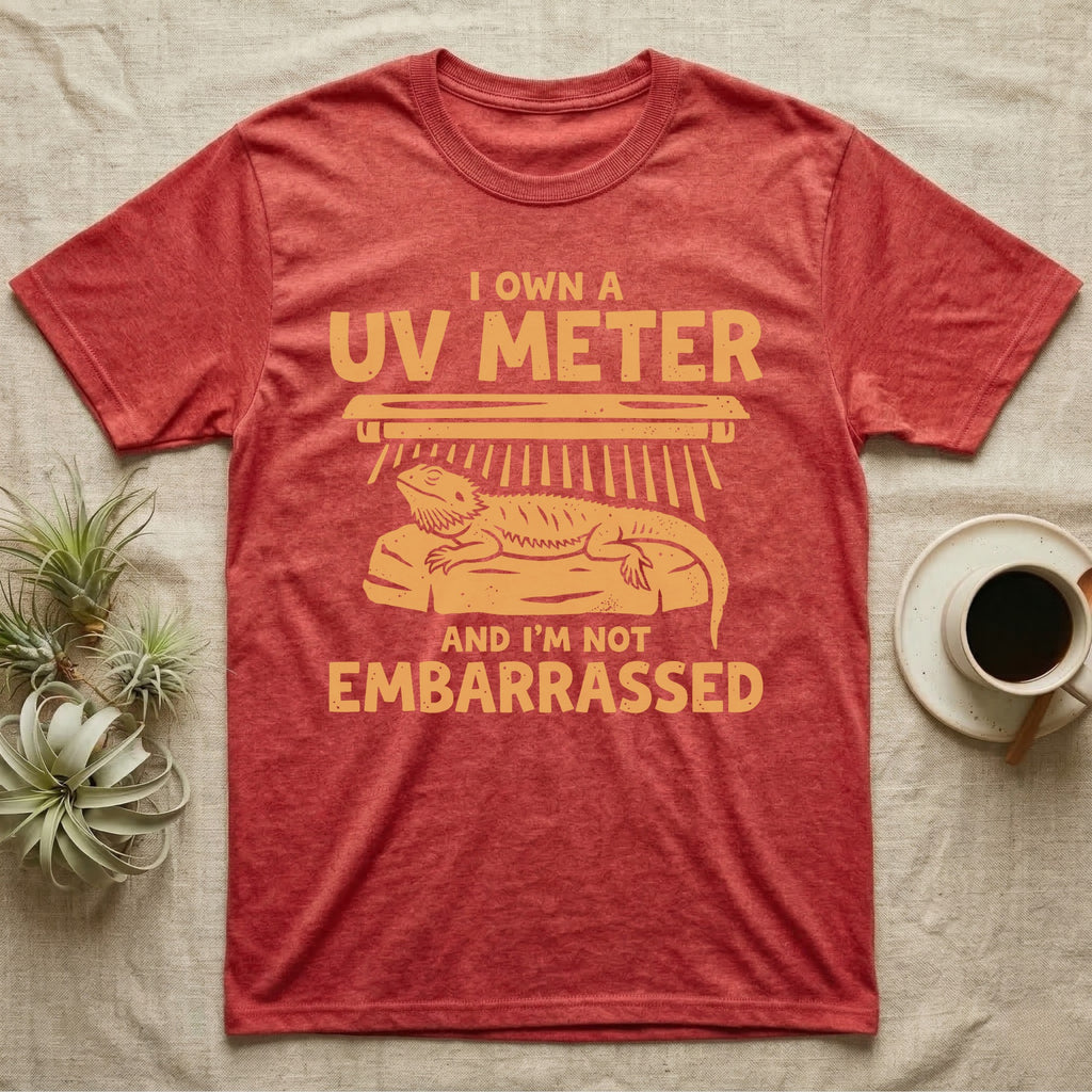 Reptile Keeper UV Meter T-Shirt in Heather Red — Linocut block-print badge of a UVB tube lamp above an empty basking rock, ringed by carved slogan lettering.