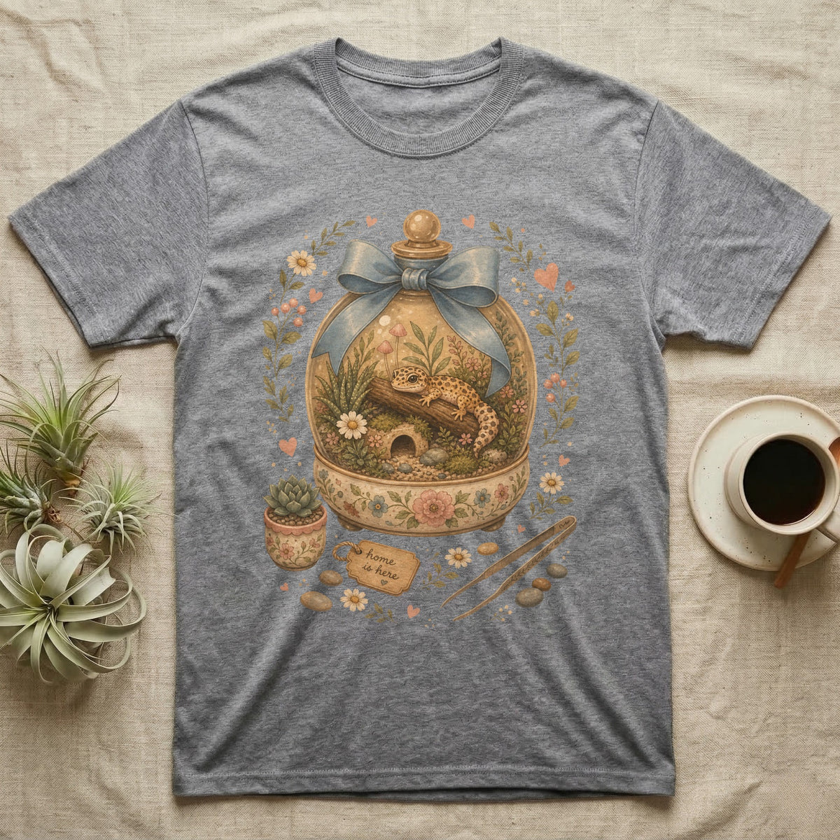 Leopard gecko in a terrarium on a grey t-shirt with "Home is here" tag.