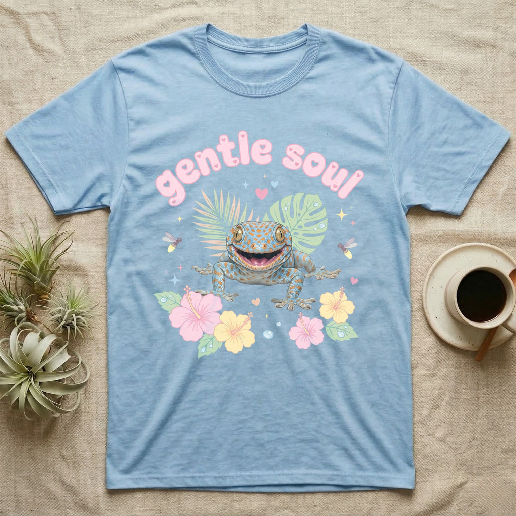 Tokay Gecko Baby T-Shirt in Light Blue — Blue-and-orange spotted tokay gecko among pastel leaves and hibiscus under puffy pink bubble text "gentle soul".