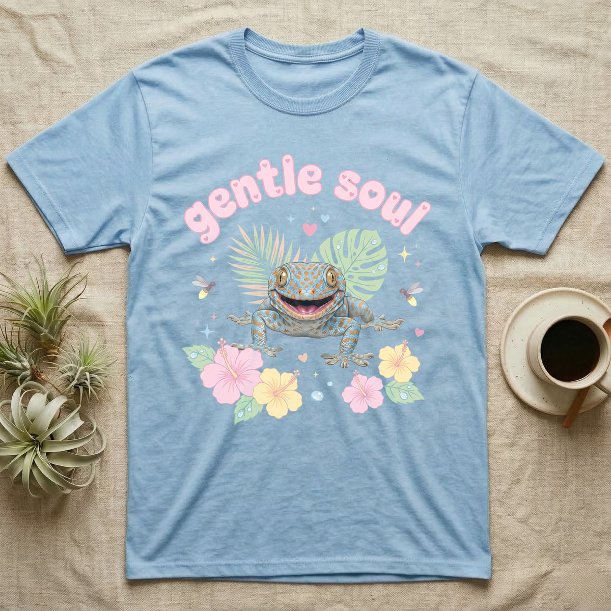 Tokay Gecko Baby T-Shirt in Light Blue — Blue-and-orange spotted tokay gecko among pastel leaves and hibiscus under puffy pink bubble text "gentle soul".