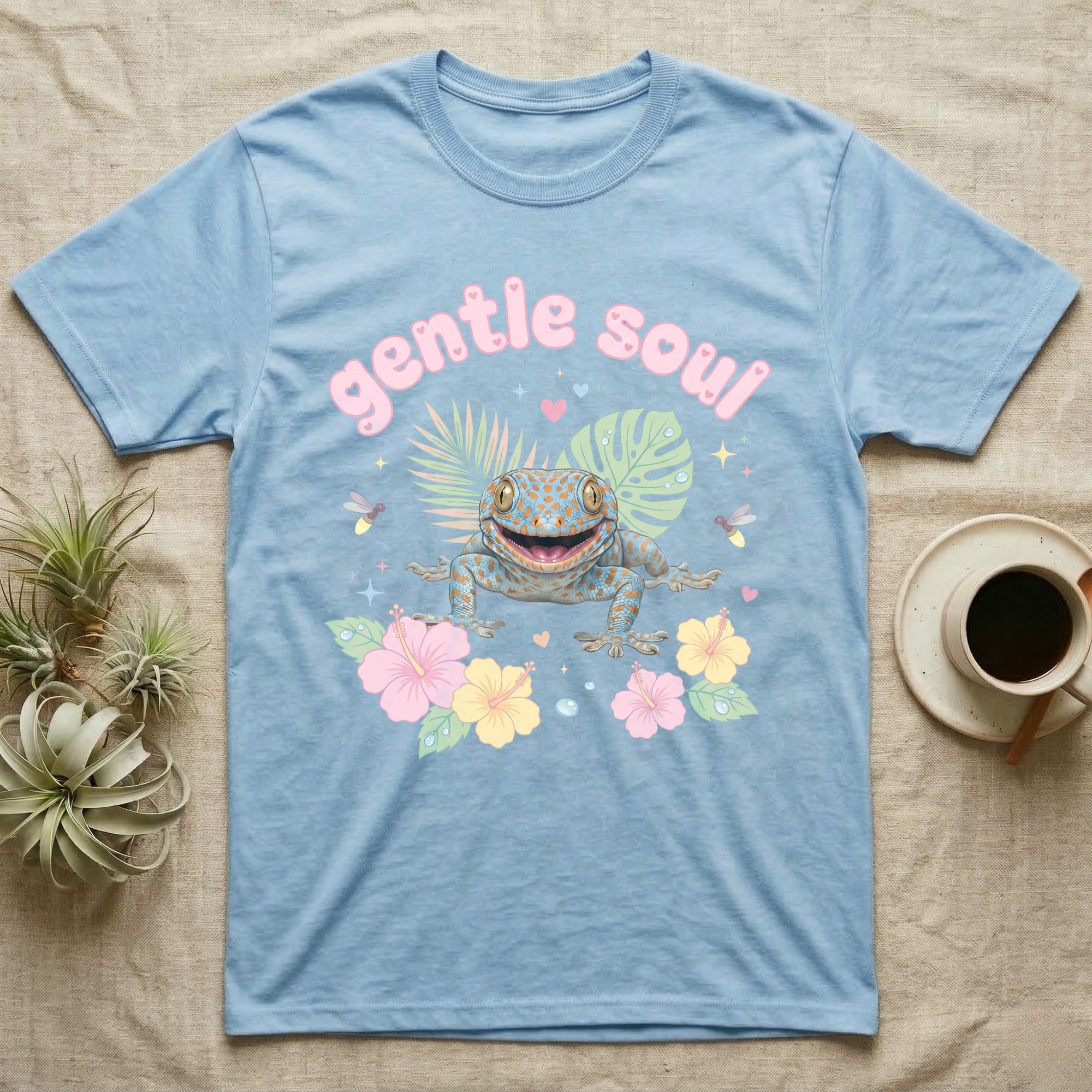 Tokay Gecko Baby T-Shirt in Light Blue — Blue-and-orange spotted tokay gecko among pastel leaves and hibiscus under puffy pink bubble text "gentle soul".