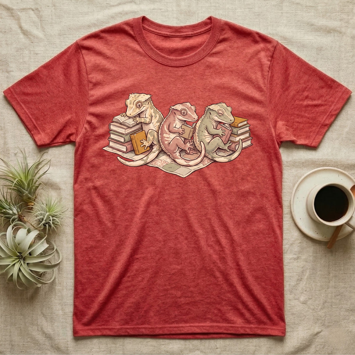 Gecko Book Club T-Shirt in Heather Red — Warm storybook illustration of three crested geckos in a cozy reading row, each beside a tiny stack of books.