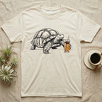 Slow Drip Tortoise T-Shirt in Natural — Flat meme-style illustration of a sulcata tortoise reaching slowly toward a tall iced slow-drip coffee.