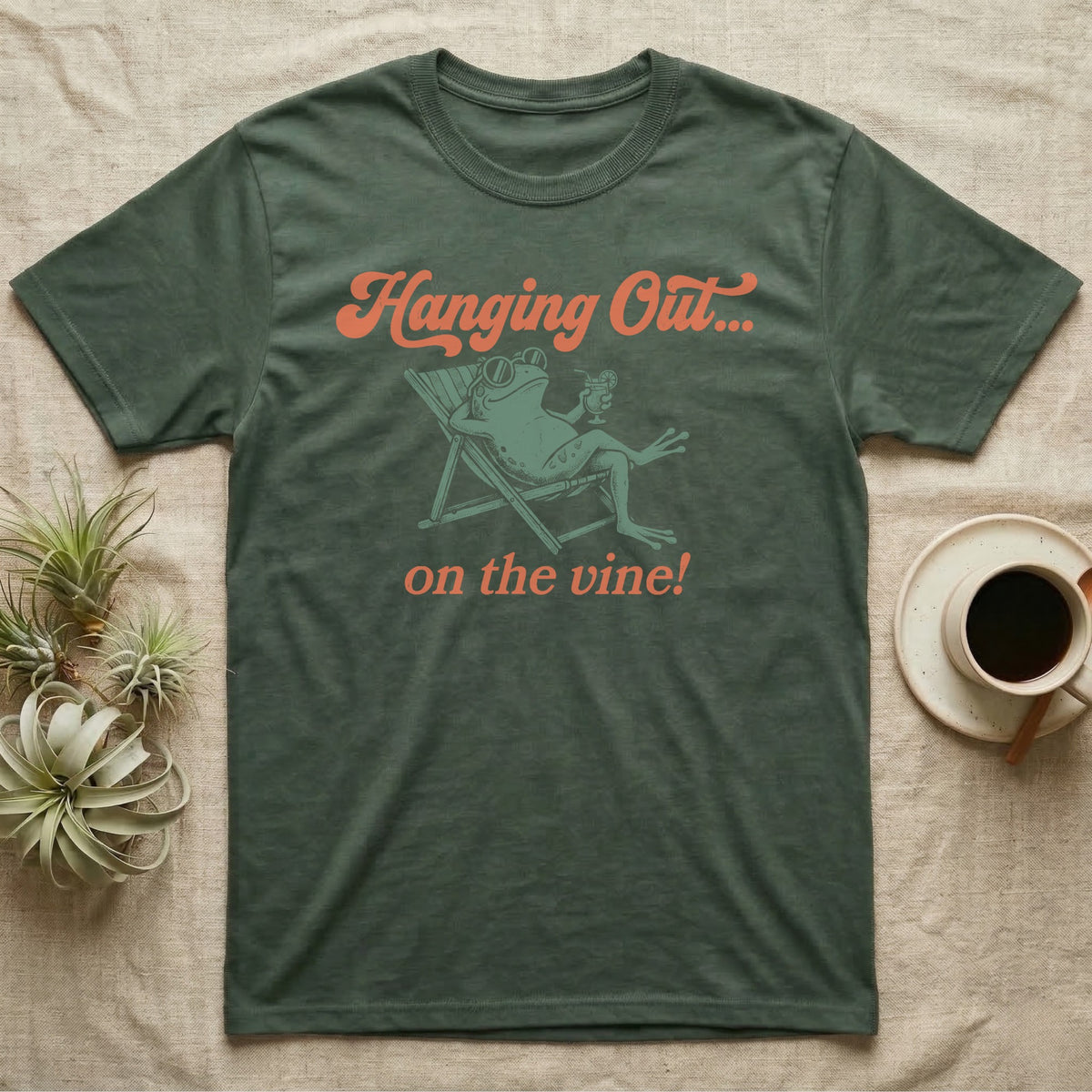 Tomato Frog Vine Vibes T-Shirt in Military Green — Illustrated tomato frog reclining in a beach chair with sunglasses and a cocktail, coral script reading Hanging Out On The Vine.