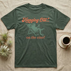 Tomato Frog Vine Vibes T-Shirt in Military Green — Illustrated tomato frog reclining in a beach chair with sunglasses and a cocktail, coral script reading Hanging Out On The Vine.