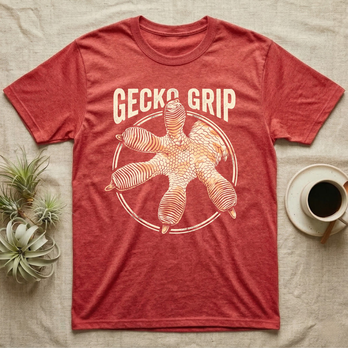 Macro badge illustration of a gecko's splayed foot with ribbed adhesive toe pads inside a distressed circular border, arched wordmark reading GECKO GRIP. — shown on a Heather Red tee.