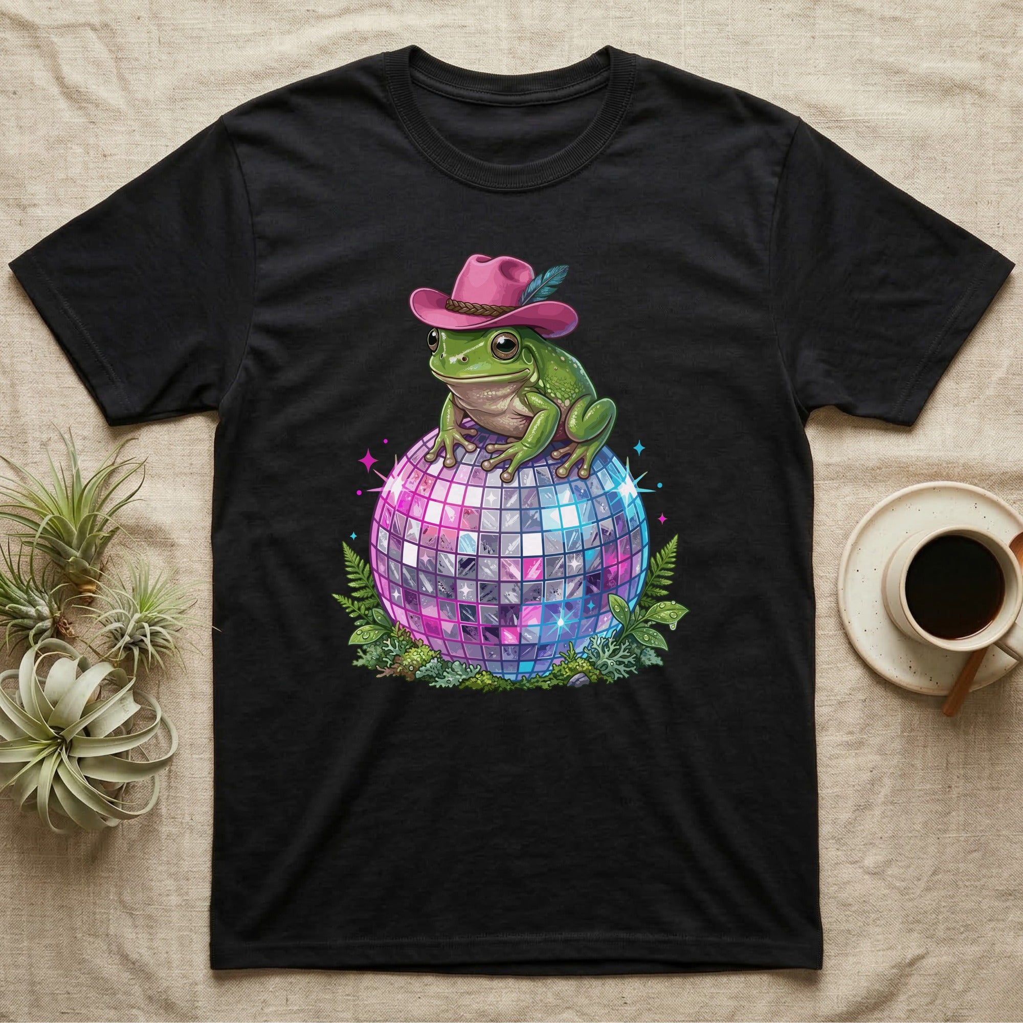 Frog wearing a pink cowboy hat sits on a disco ball surrounded by ferns.