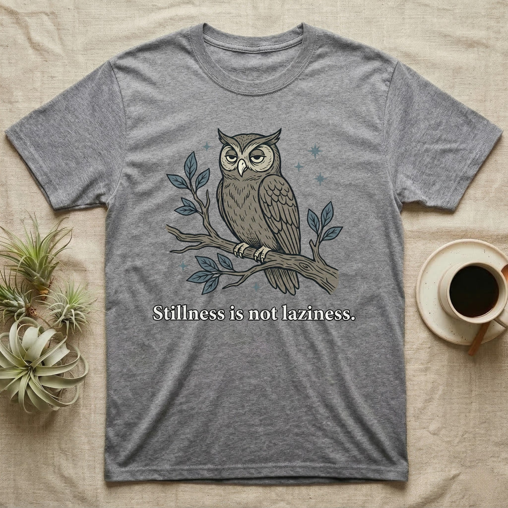 Gray t-shirt with an owl perched on a branch, text reads "Stillness is not laziness."