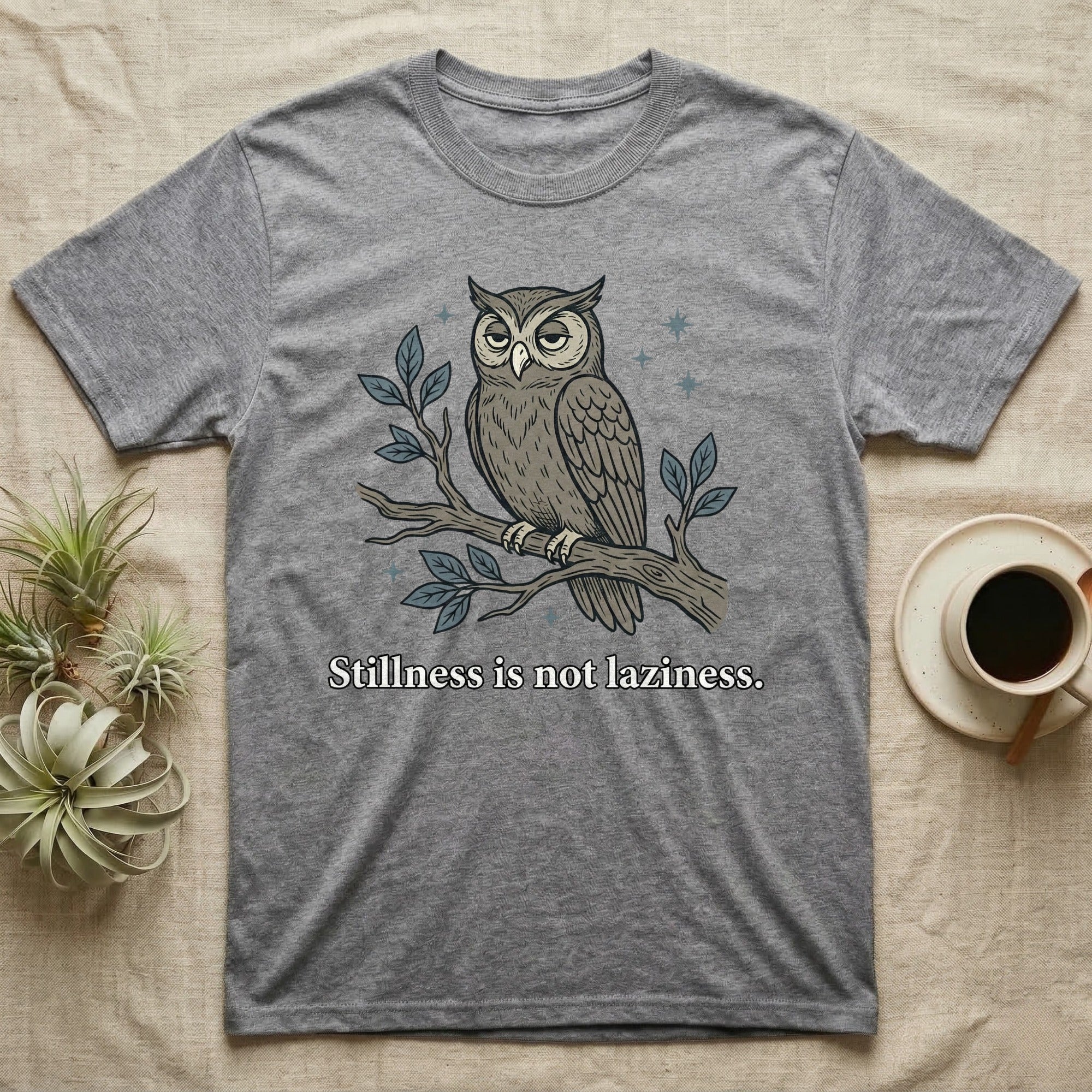 Gray t-shirt with an owl perched on a branch, text reads "Stillness is not laziness."