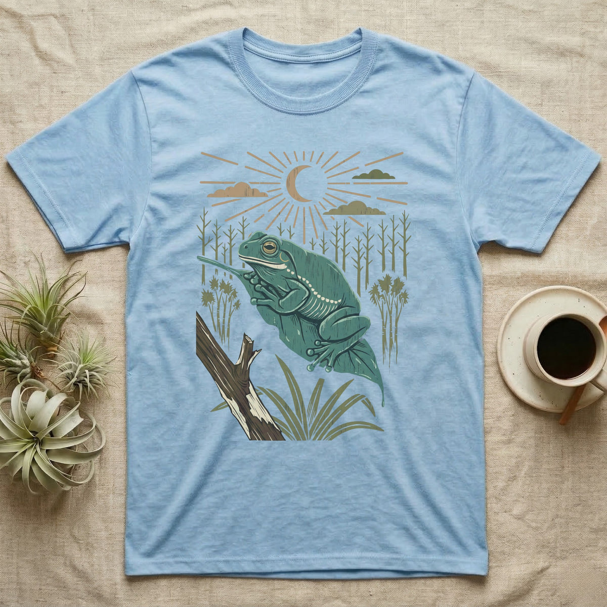 White's Tree Frog Home Range T-Shirt in Light Blue — Woodcut-style illustration of a White's tree frog resting on a broad wet leaf with reed stems and a crescent moon behind, no on-shirt text.