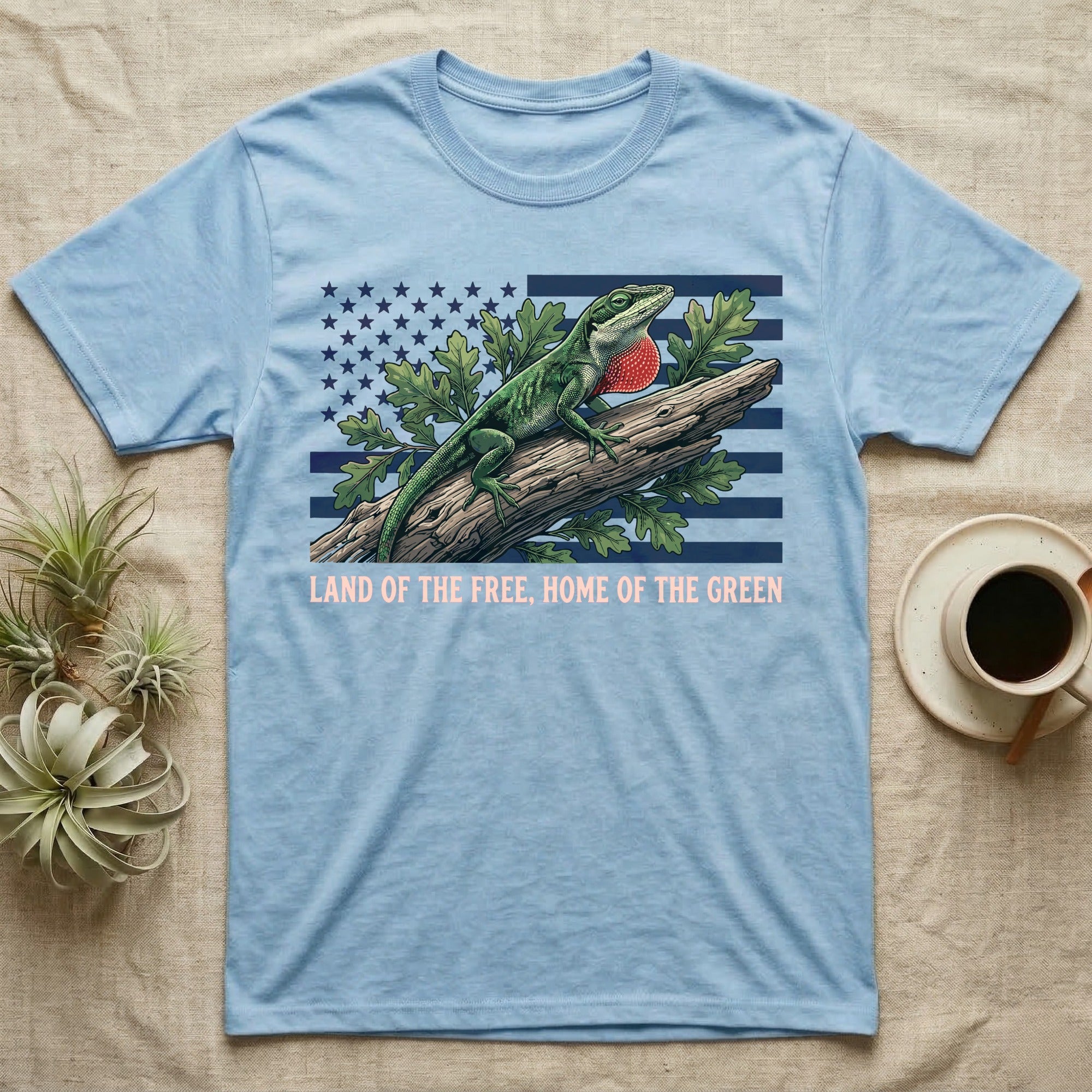 Green Anole 1776 T-Shirt in Light Blue — Realistic green anole with a red dewlap on a branch over a distressed flag under text Land of the Free, Home of the Green.