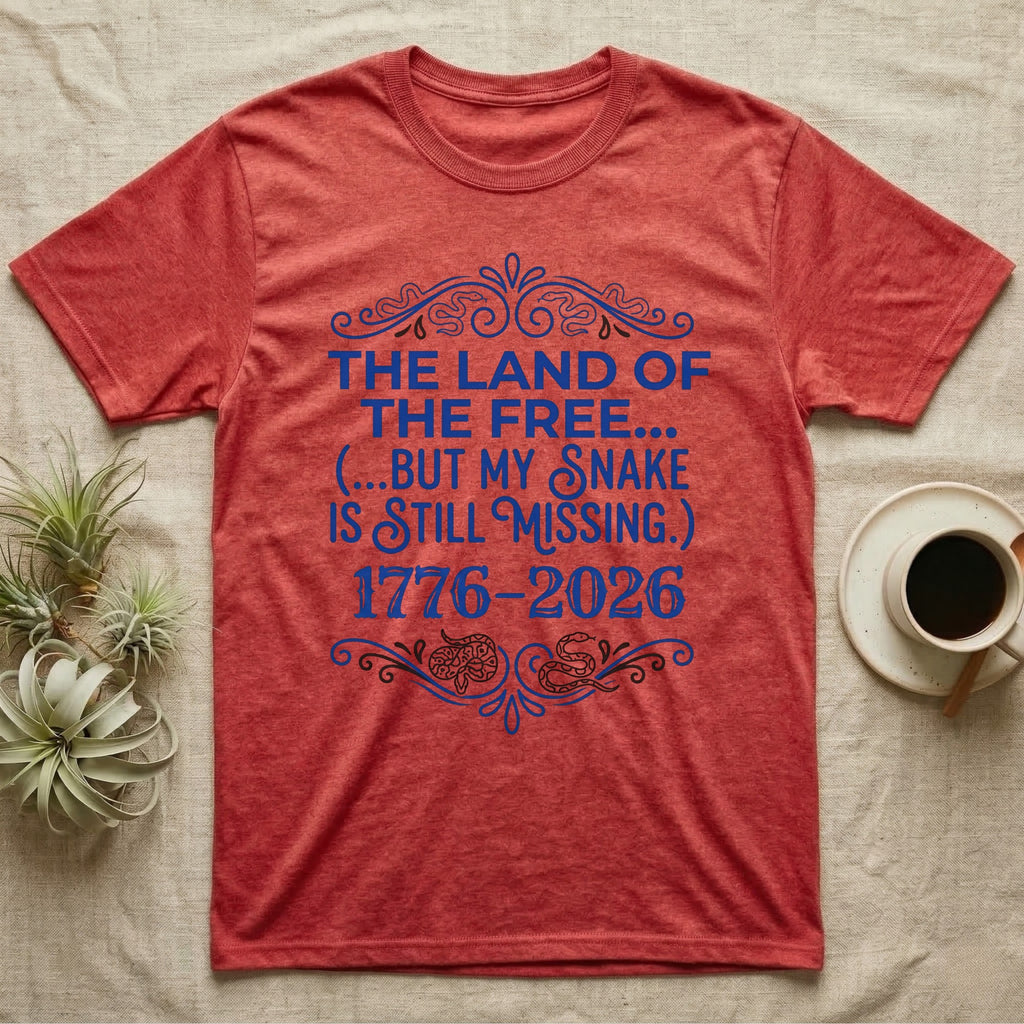 Corn Snake Still Missing Tee in Heather Red — Royal blue typographic tee reading The land of the free but my snake is still missing, with Victorian filigree and small coiled corn snakes.