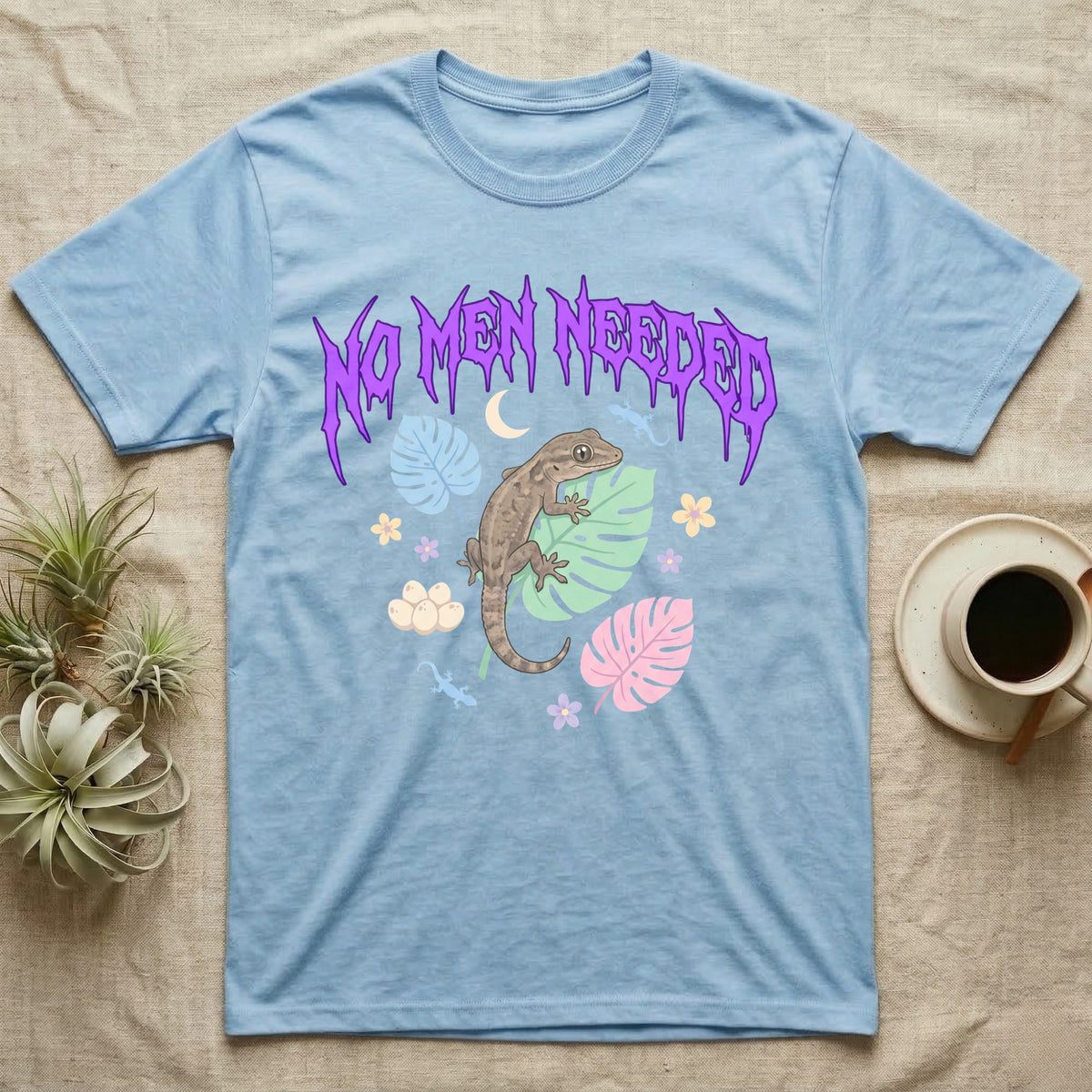 Mourning Gecko Feral T-Shirt in Light Blue — Mourning gecko on a leaf flanked by clone silhouettes under a jagged violet metal "NO MEN NEEDED" wordmark.
